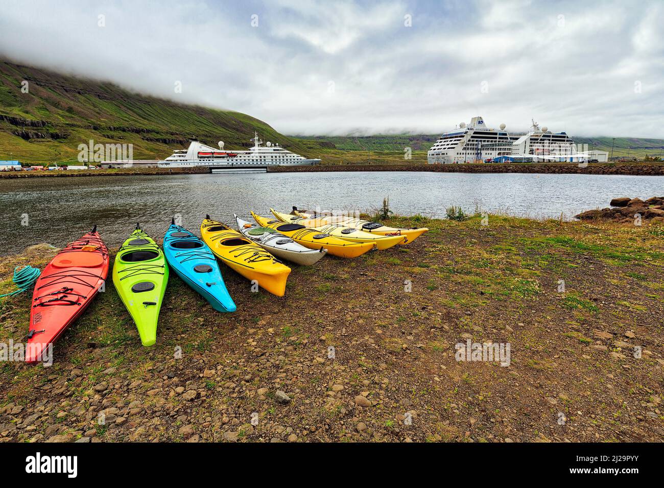 Bunte Kajaks am Ufer des Fjords, Kreuzschiff in Seyoisfjoerour, Seydisfjoerdur, Ostisland, Island Stockfoto