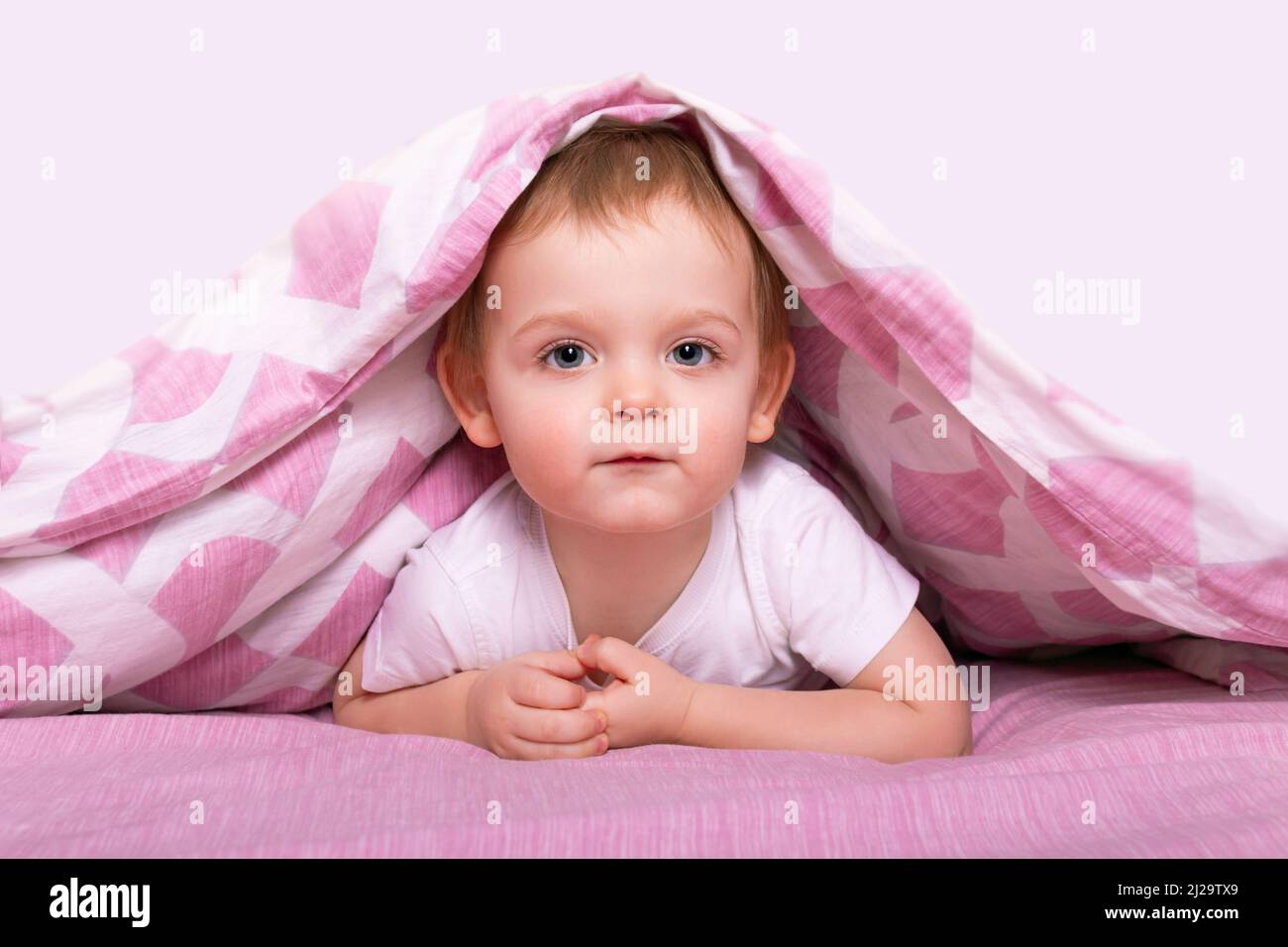 Kleiner kaukasischer Junge, der sich unter einer rosa Decke versteckt. Stockfoto