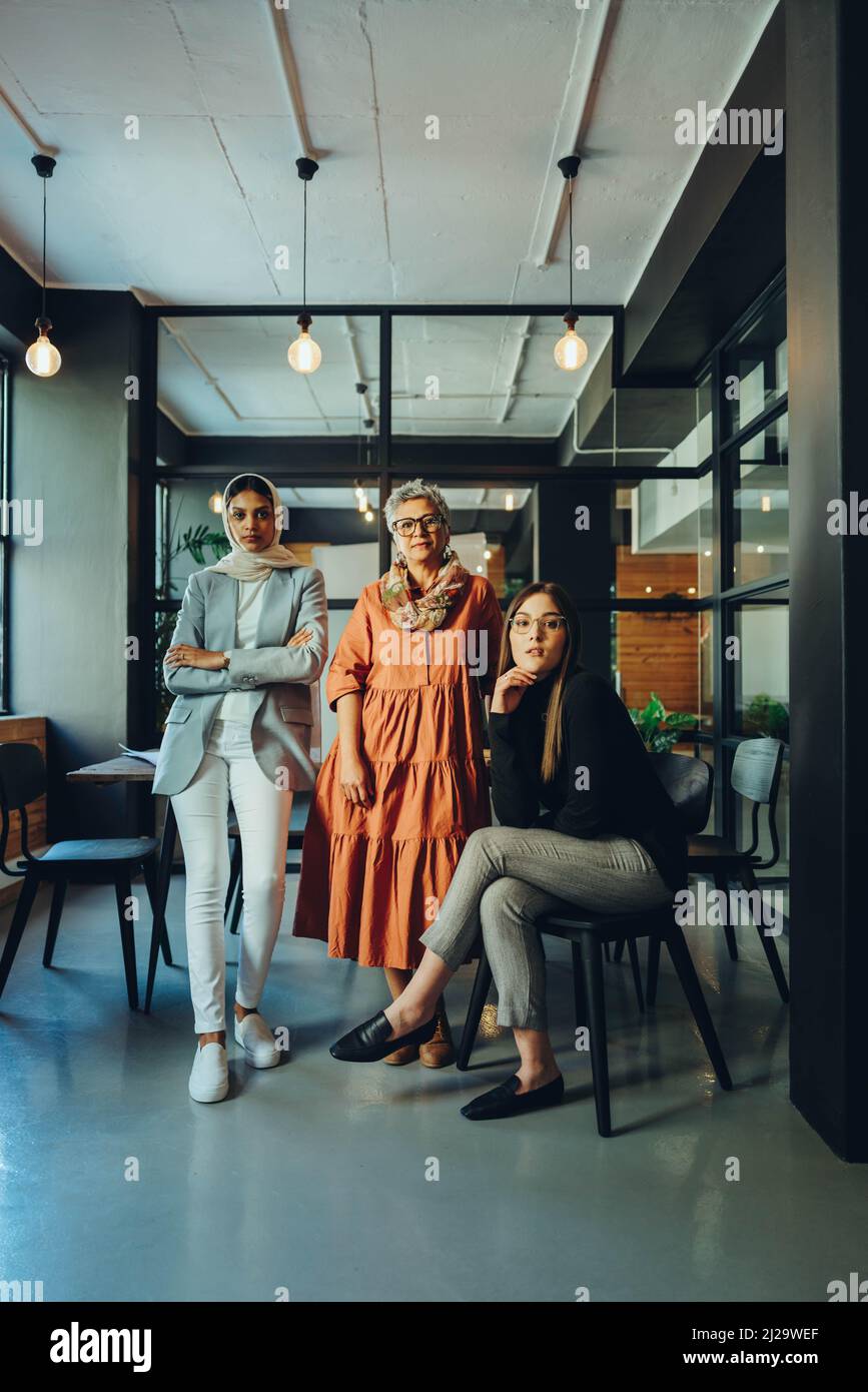 Eine Gruppe verschiedener Geschäftsfrauen, die in einem Büro auf die Kamera schauen. Drei multikulturelle Unternehmer, die als Team an einem integrativen Arbeitsplatz arbeiten. Konf Stockfoto