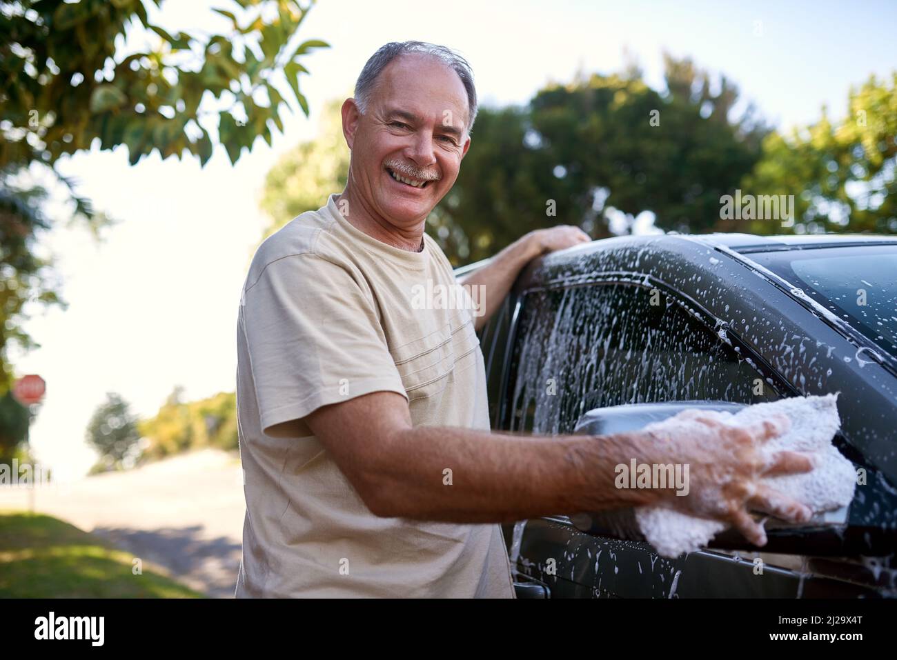 Sich um sein Auto kümmern. Porträt eines Mannes, der draußen ein Auto wäscht. Stockfoto