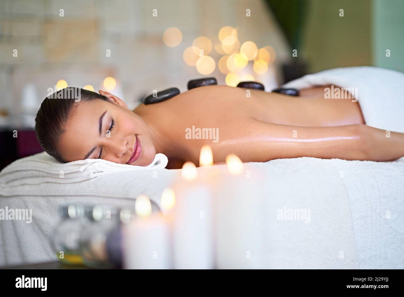 Gönnen Sie sich einen Urlaub auf unserem Massagetisch. Aufnahme einer jungen Frau, die in einem Spa eine Hot Stone Massage genießt. Stockfoto