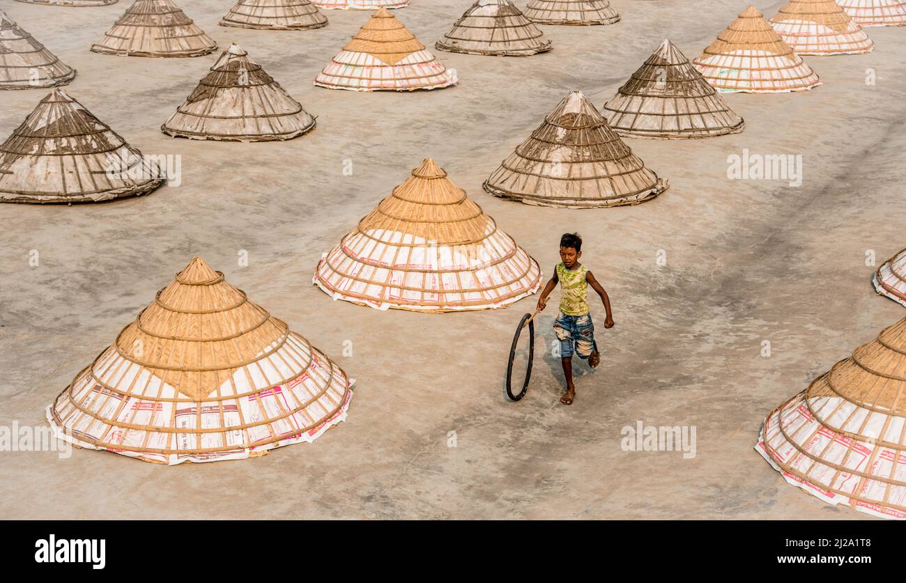 Brahmanbaria, Chittagong, Bangladesch. 31. März 2022. Kinder laufen und spielen zwischen Hunderten traditioneller Reismühlen aus Bambus.nach dem Kochen wird das Getreide von Arbeitern in Haufen gefegt und bis zu acht Stunden lang in Brahmanbaria, Bangladesch, getrocknet. Die Reismühlenarbeiter begannen ihre Arbeit von sehr früh morgens von 5 bis 2pm Uhr täglich. Nach der Mittagspause spielen die Kinder der Arbeiter ihre Nachmittagsspiele mit Freunden in diesem Reismühlenfeld. (Bild: © Mustasinur Rahman Alvi/ZUMA Press Wire) Bild: ZUMA Press, Inc./Alamy Live News Stockfoto