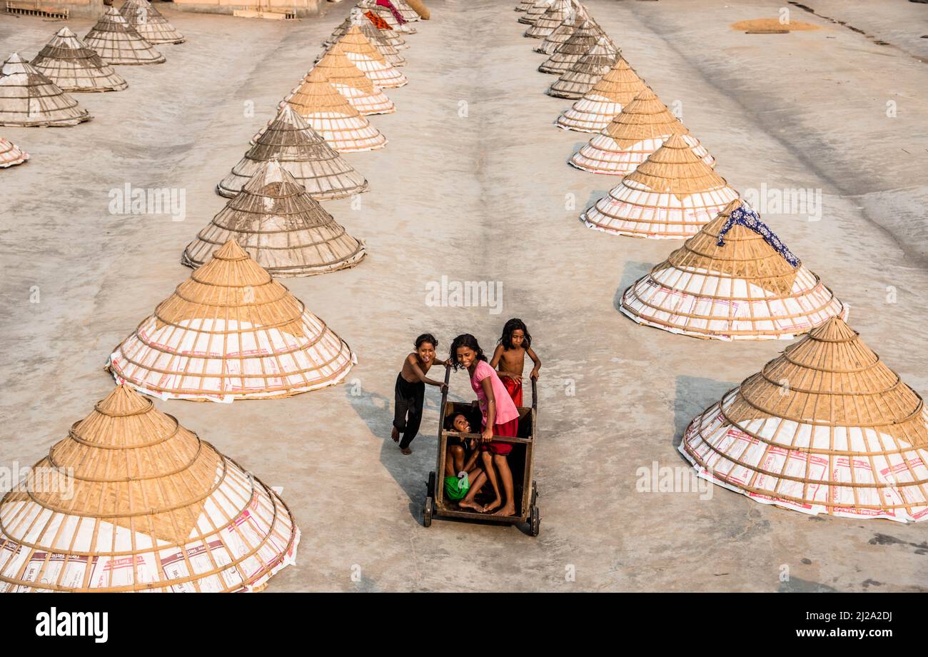 Brahmanbaria, Chittagong, Bangladesch. 31. März 2022. Kinder laufen und spielen zwischen Hunderten traditioneller Reismühlen aus Bambus.nach dem Kochen wird das Getreide von Arbeitern in Haufen gefegt und bis zu acht Stunden lang in Brahmanbaria, Bangladesch, getrocknet. Die Reismühlenarbeiter begannen ihre Arbeit von sehr früh morgens von 5 bis 2pm Uhr täglich. Nach der Mittagspause spielen die Kinder der Arbeiter ihre Nachmittagsspiele mit Freunden in diesem Reismühlenfeld. (Bild: © Mustasinur Rahman Alvi/ZUMA Press Wire) Bild: ZUMA Press, Inc./Alamy Live News Stockfoto