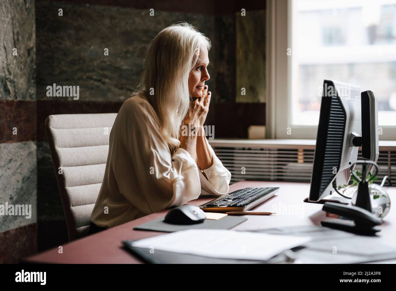 Anwältin mit langen weißen Haaren starrt im Büro auf den Computer Stockfoto