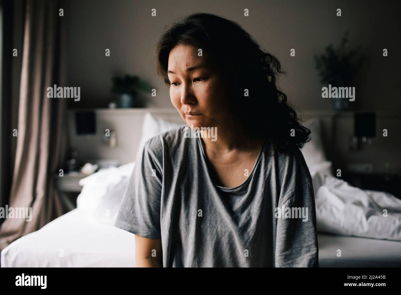 Einsame depressive Frau, die zu Hause im Schlafzimmer sitzt und hinunterschaut Stockfoto