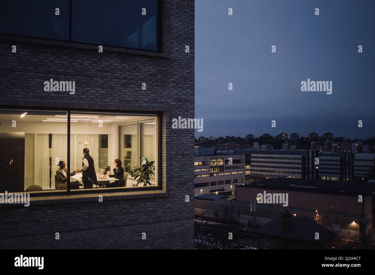 Mehrrassische weibliche Kollegen, die spät arbeiten, werden durch das Fenster am Arbeitsplatz gesehen Stockfoto