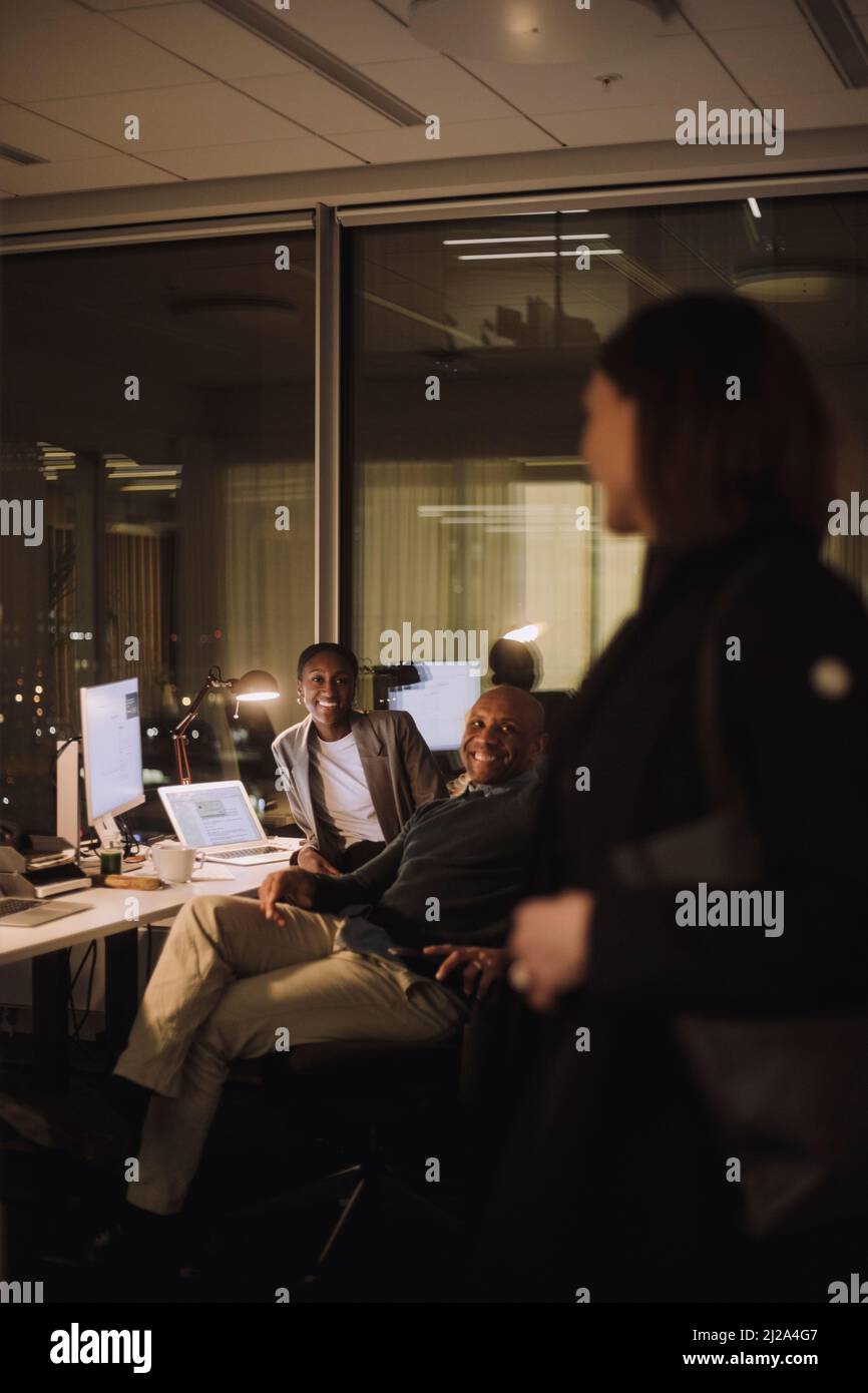 Glückliche weibliche und männliche Kollegen, die am Arbeitsplatz mit einer Geschäftsfrau sprechen Stockfoto