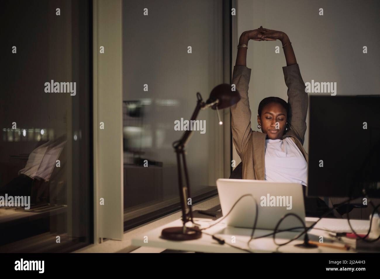 Müde Geschäftsfrau, die sich die Hände streckt, während sie nachts im Büro arbeitet Stockfoto