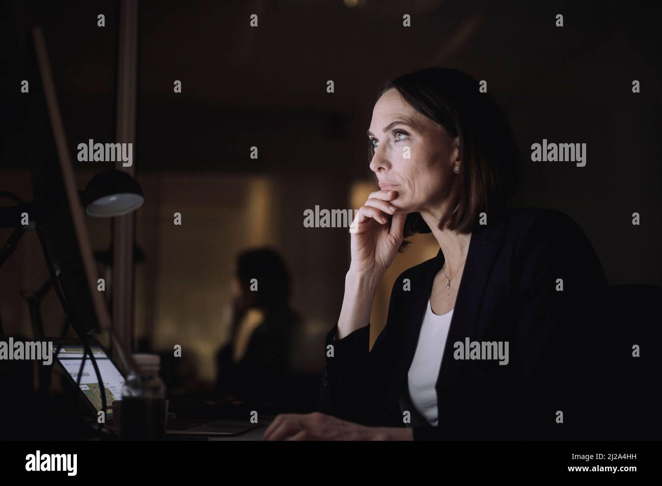 Reife Geschäftsfrau mit Hand am Kinn, die am Arbeitsplatz über dem Computer arbeitet Stockfoto