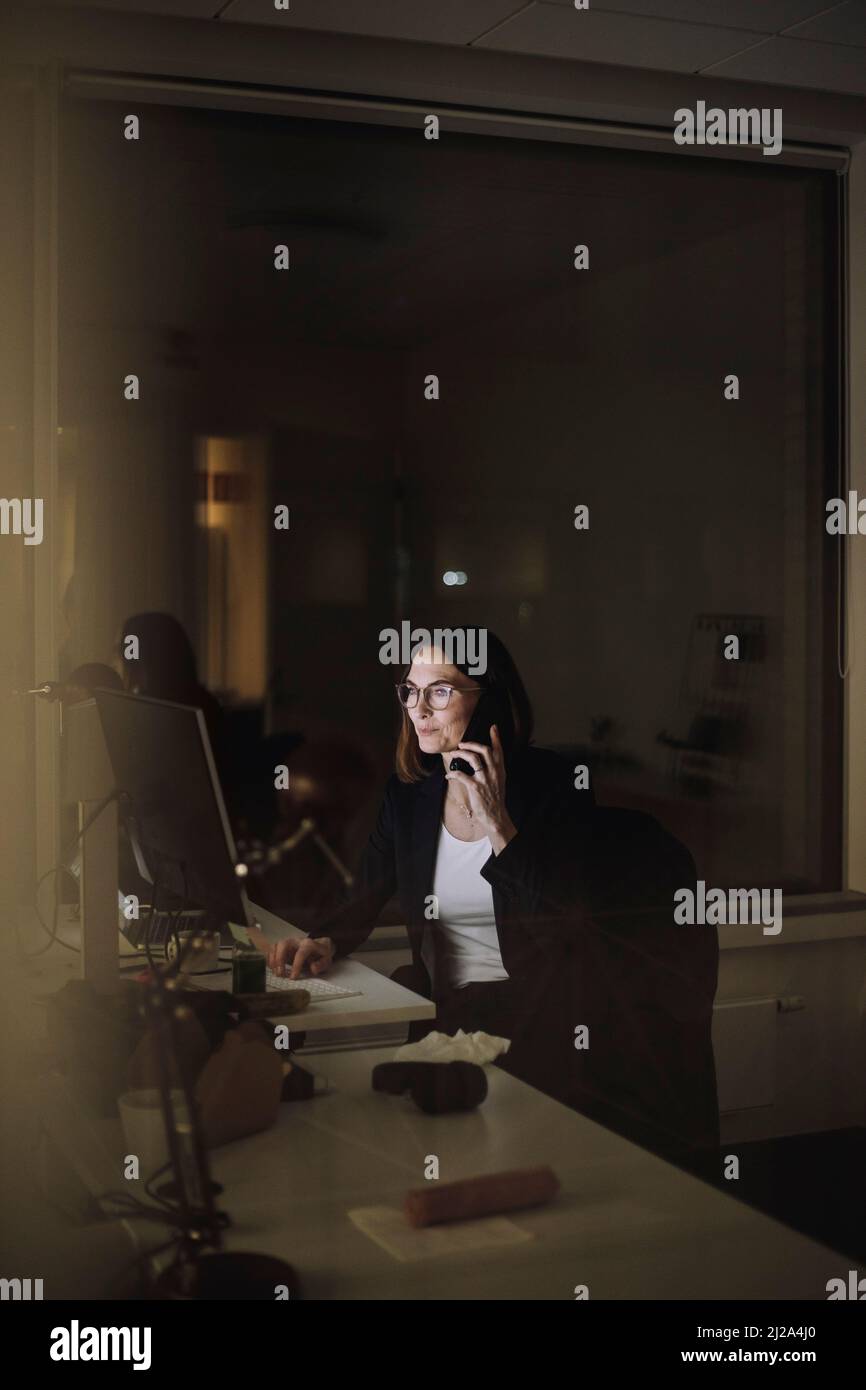 Reife Geschäftsfrau, die spät im Büro mit dem Smartphone spricht Stockfoto