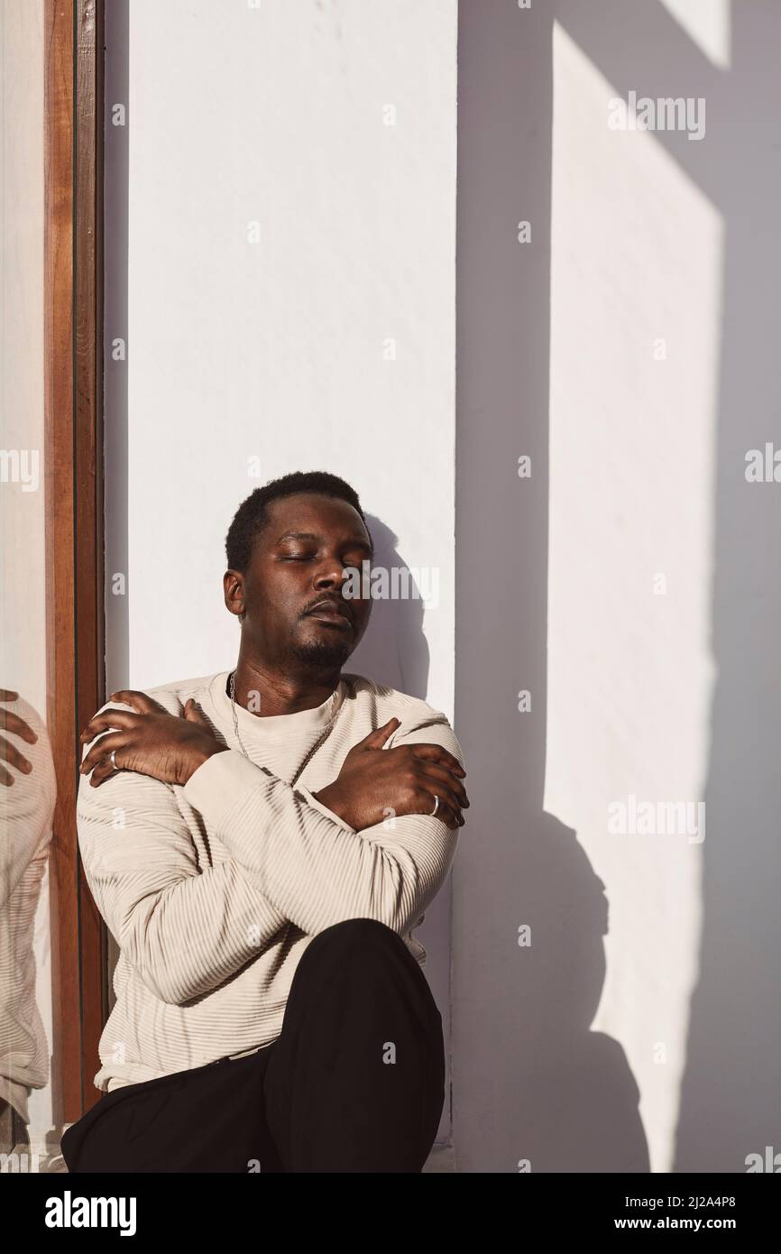 Ein mittelerwachsener Mann umarmt sich an der weißen Wand Stockfoto