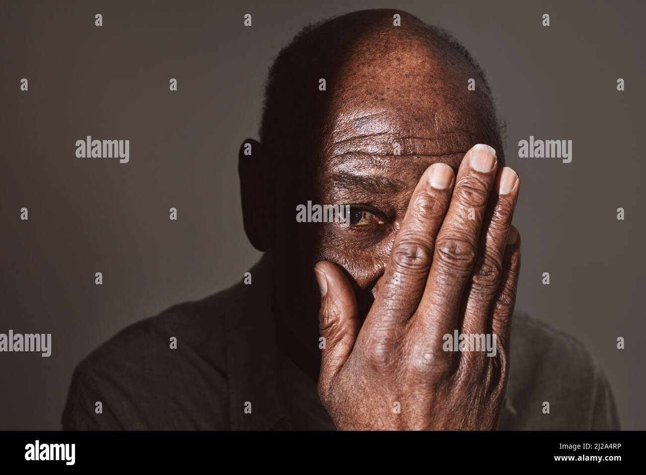 Älterer Mann, der im Studio Auge mit der Hand bedeckt Stockfoto