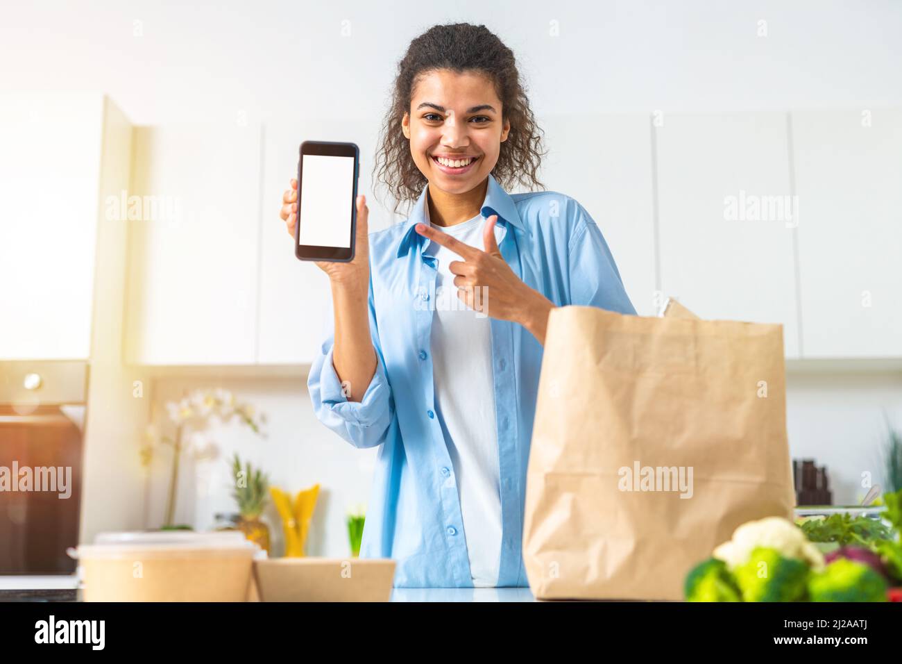 Lächelnde Frau mit einer Einkaufstasche, die online über das Smartphone bestellt und direkt zu Hause geliefert wurde Stockfoto