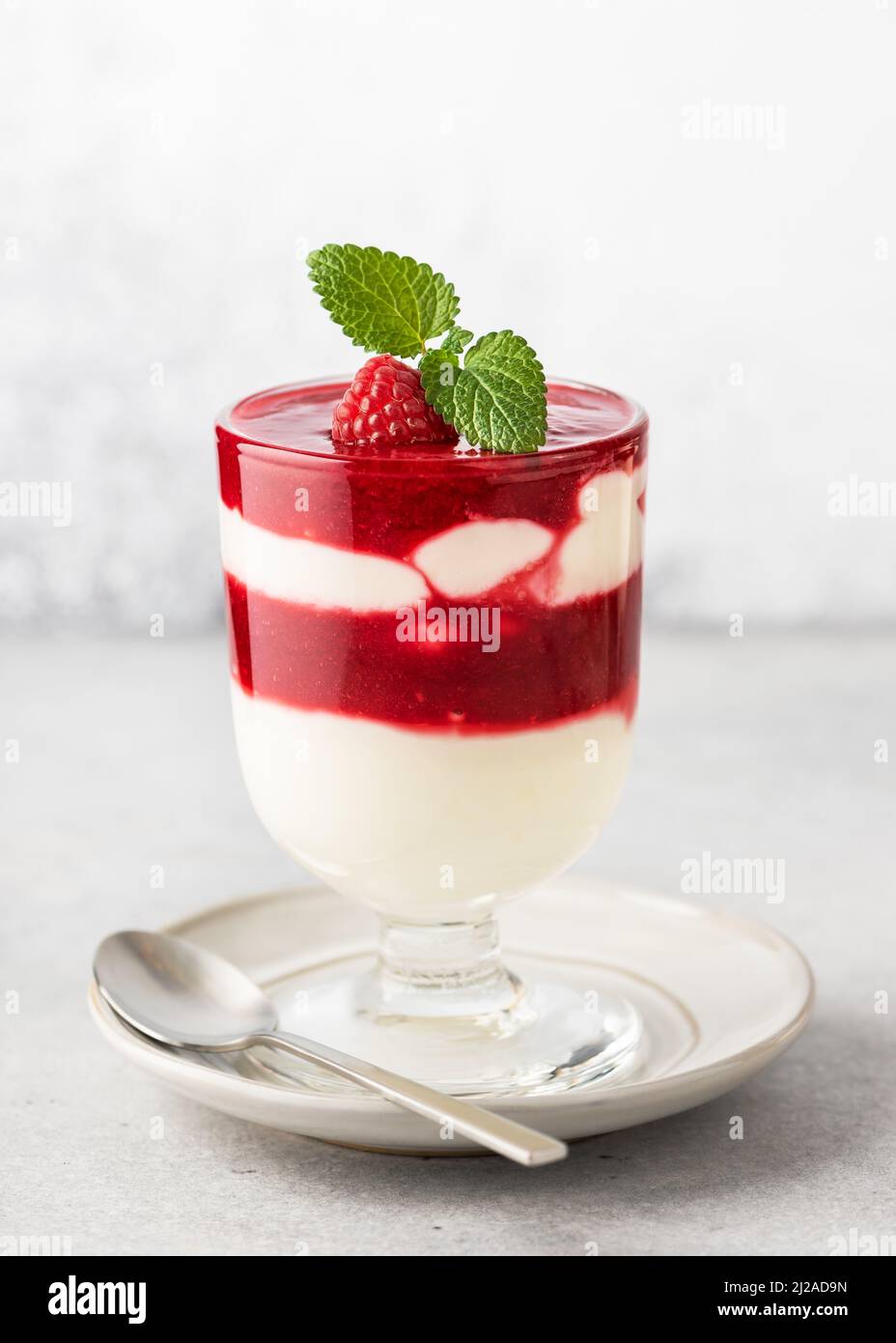 Ein Glas hausgemachtes Obst-Dessert mit Buttermilchcreme, Himbeersauce-Schichten und frischen Zitronenmelisse-Blättern garnieren. Stockfoto