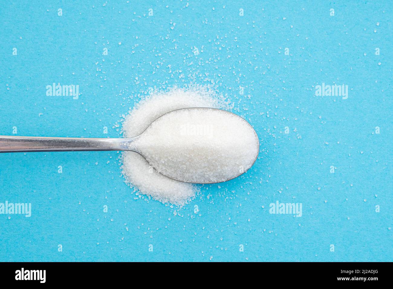 Nahaufnahme eines Löffels mit Zuckerhaufen, Kristalle aus weißem Zucker auf blauem Hintergrund, Draufsicht Stockfoto