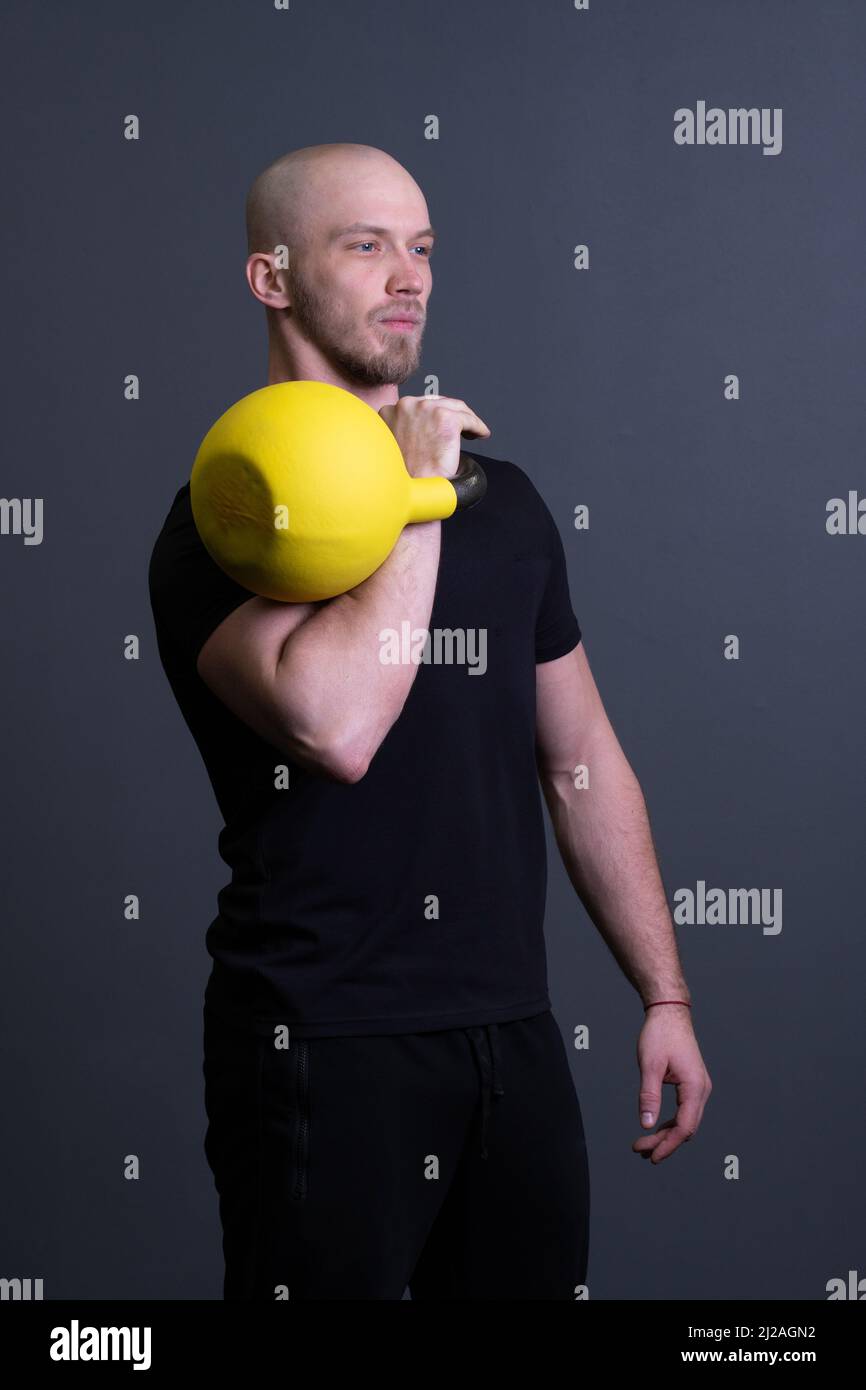 Kerl mit einer gelben Kettlebell-Fitnessstudio anonyme Trainingsstärke, am Nachmittag Motivation Bemühungen von Kommissionierung aus Gummi Jugend, südöstliche Aktivität Stockfoto