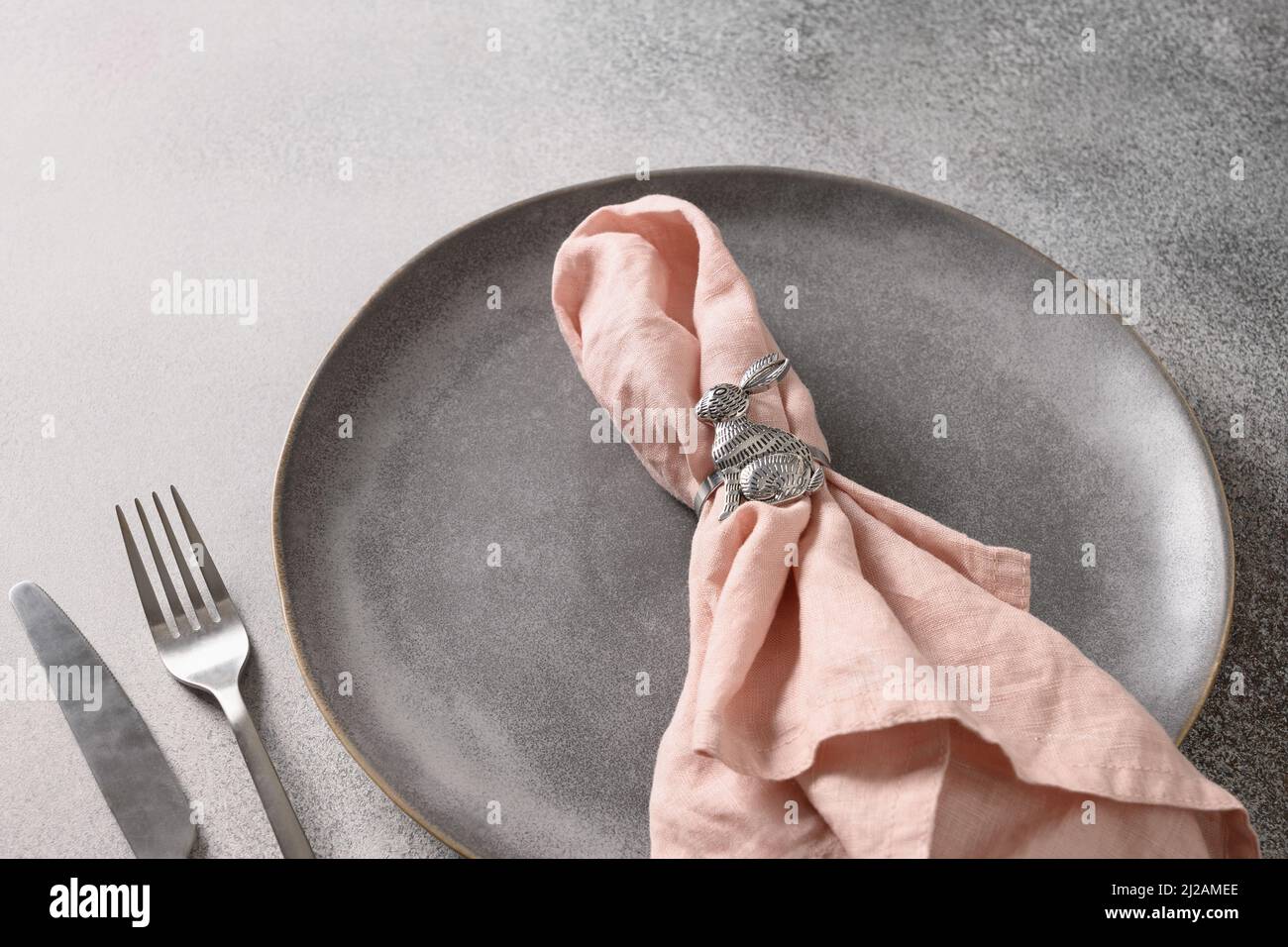 Osteressen und Tischdekoration mit rosa Dekorationen und Kaninchen als Serviettenring auf grauem Hintergrund. Nahaufnahme. Speicherplatz kopieren. Stockfoto