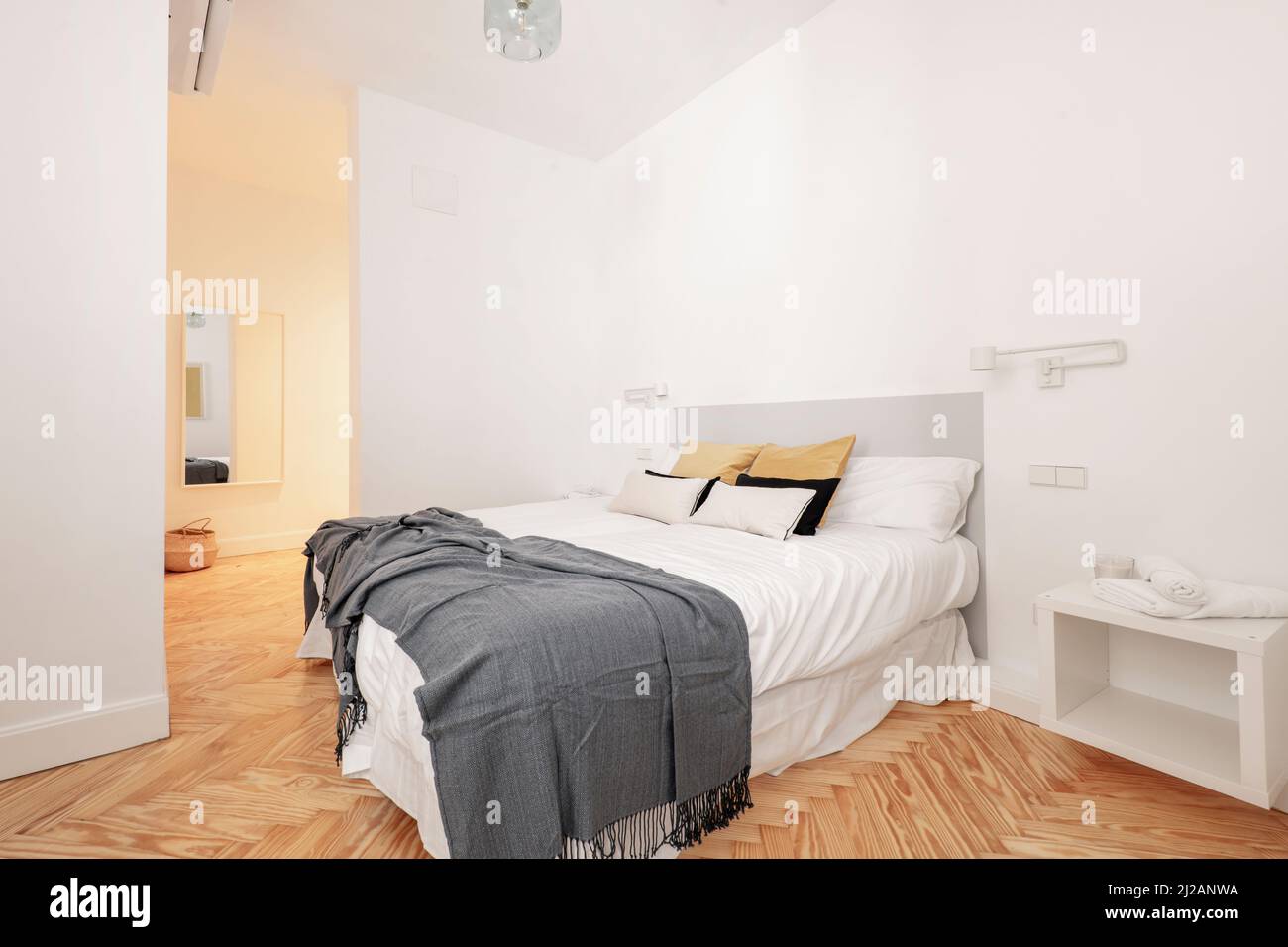 Schlafzimmer mit großem Bett mit vielen Kissen, zwei Nachttischen mit einziehbaren Lampen, weiße Zimmerei an den Türen, Kommode mit Spiegel und Klimaanlage Stockfoto