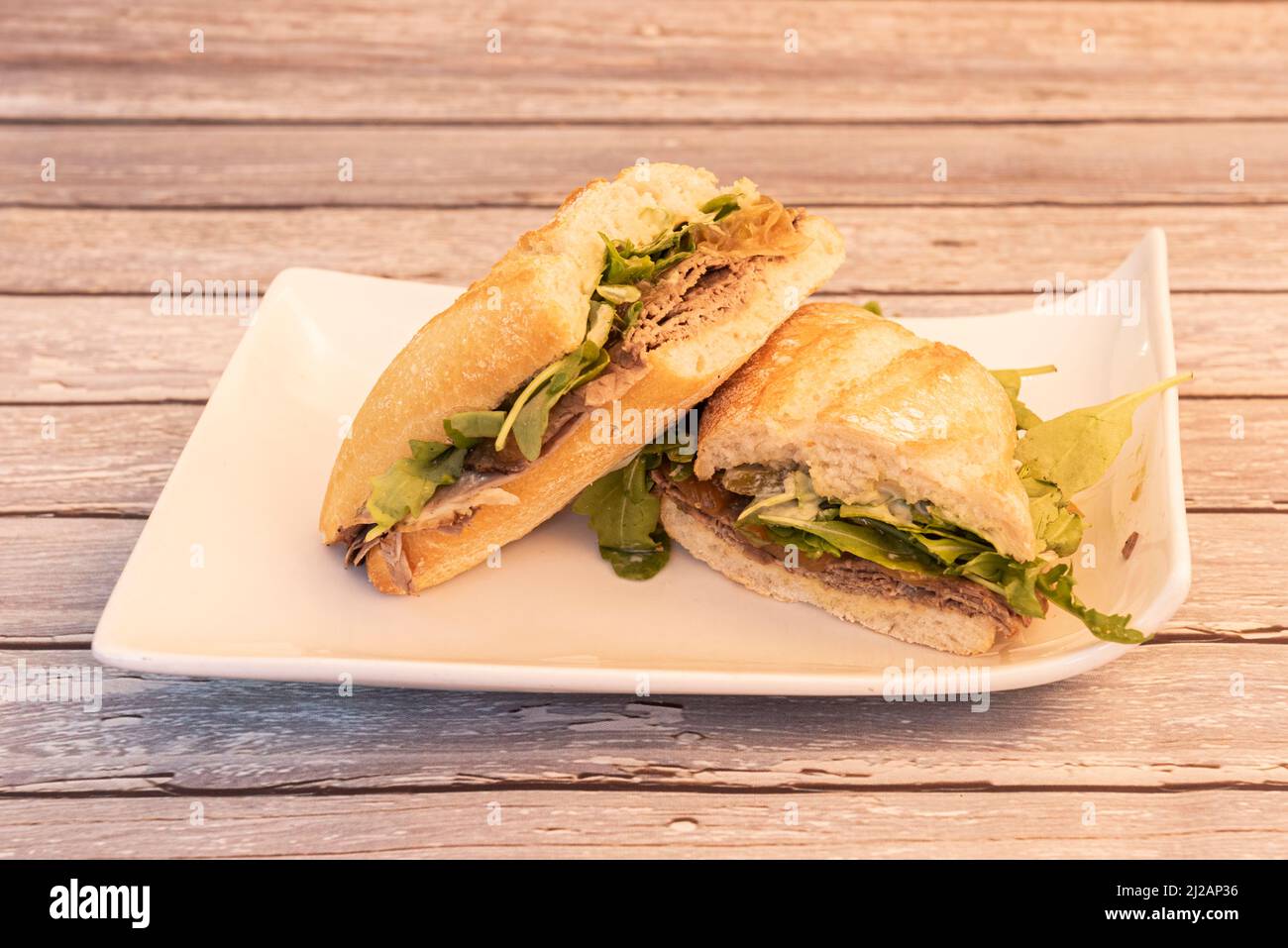 Roastbeef-Sandwich mit Rucola und Sauce mit karamellisierten Zwiebeln auf weißem Teller Stockfoto