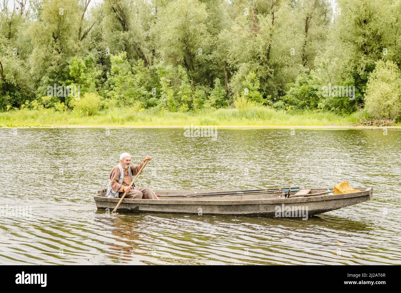 Ein Sportfischer reitet mit Hilfe eines Ruder auf einem Teich in einem Holzboot. Stockfoto