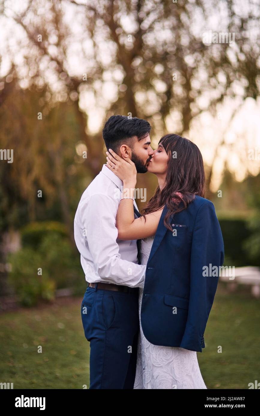 Ich könnte Euch tausendmal mehr küssen. Eine kurze Aufnahme einer anhänglichen jungen Braut, die ihren Bräutigam küsst, während sie am Hochzeitstag seine Jacke trägt. Stockfoto