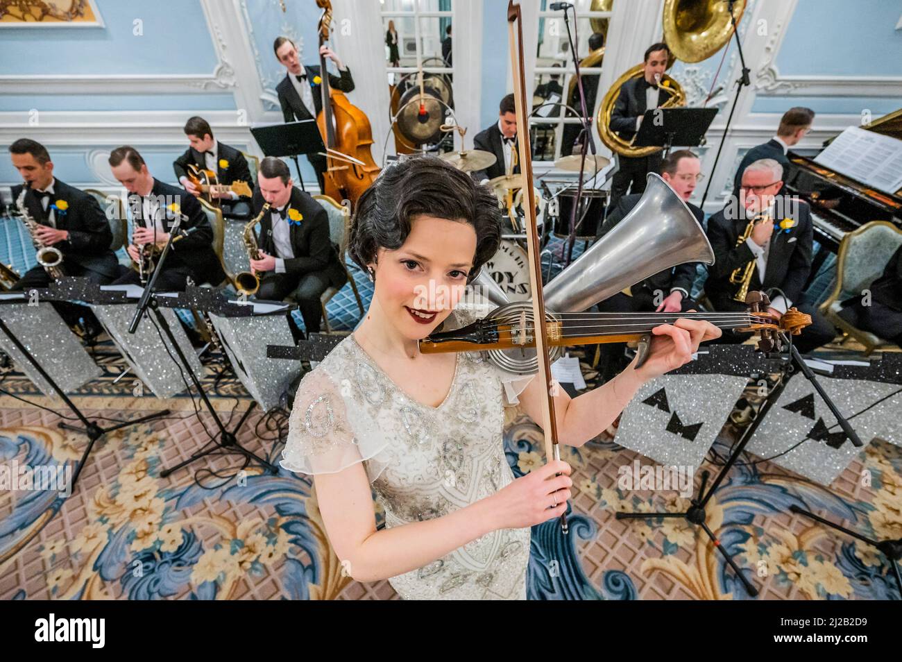 London, Großbritannien. 31 März 2022. Rebecca Smith spielt die Stroh-Geige in einem nachgebauten Vintage-Kleid - das Savoy vereint Kräfte mit Alex Mendham und seinem Orchester, um Gelder für die Ukraine zu sammeln. In den Jahren 1920s und 1930s waren die Savoy-Verhoerenen ein bekannter Name, und für diese karitative Zusammenarbeit wird das Orchester zu ‘The New Savoy-Verhoerenden' und eine exklusive Aufnahme im Hotel schaffen. Sie spielen im Lancaster Ballroom des Hotels, um ein Medley von Stücken aufzunehmen, die die feinsten Melodien des Jazz-Zeitalters darstellen, mit der Absicht, wertvolle Gelder für das Disasters Emergency Committee zu sammeln. Cr Stockfoto