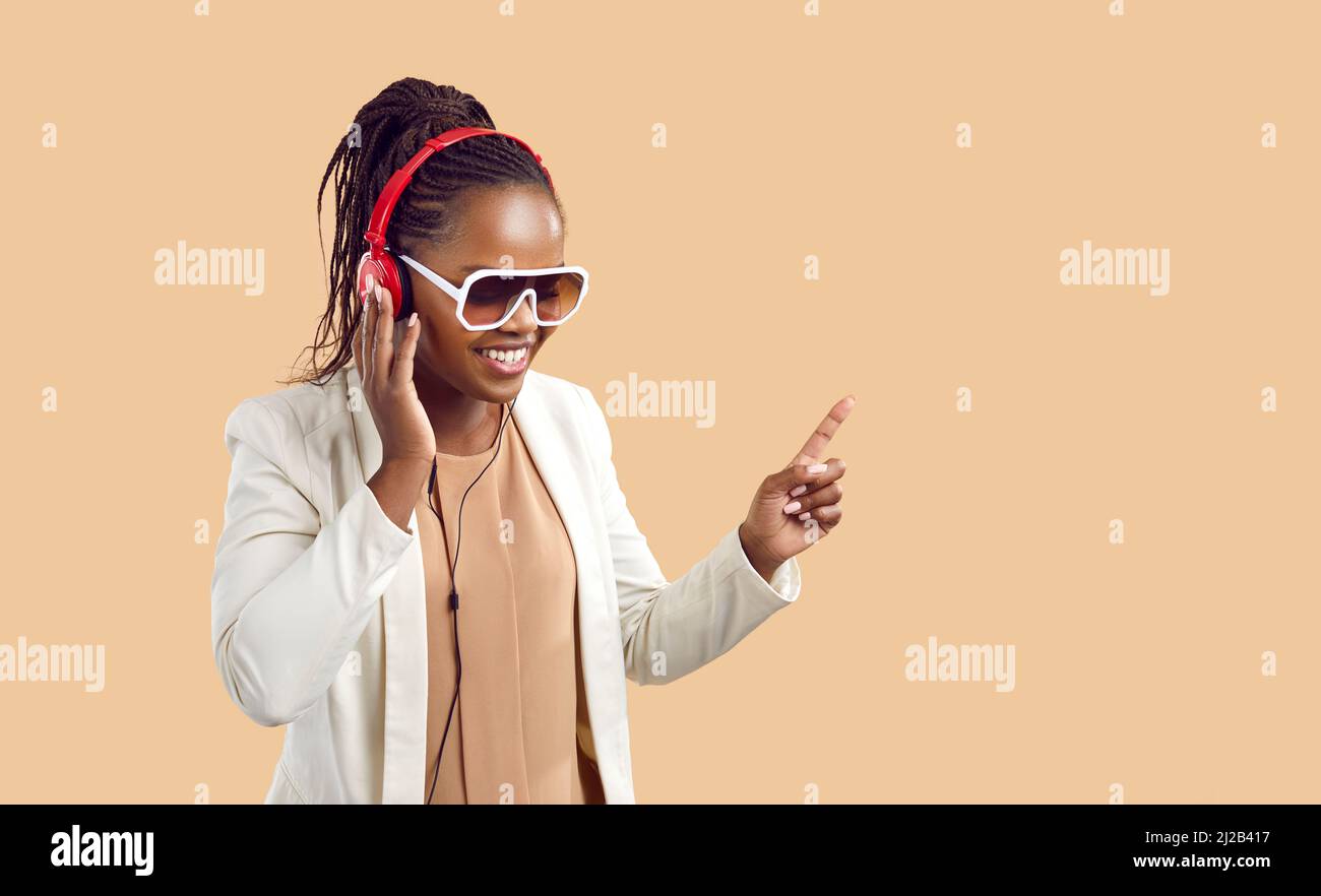 Glückliche junge afroamerikanische Frau in Kopfhörern hört Musik auf beigem Hintergrund. Stockfoto