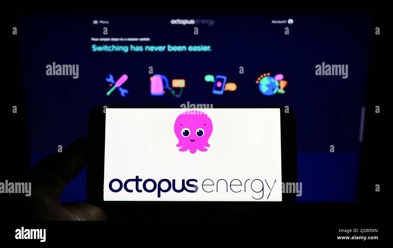 Person mit Mobiltelefon und Logo des britischen Unternehmens Octopus Energy Group für erneuerbare Energien auf dem Bildschirm vor der Webseite. Konzentrieren Sie sich auf die Telefonanzeige. Stockfoto