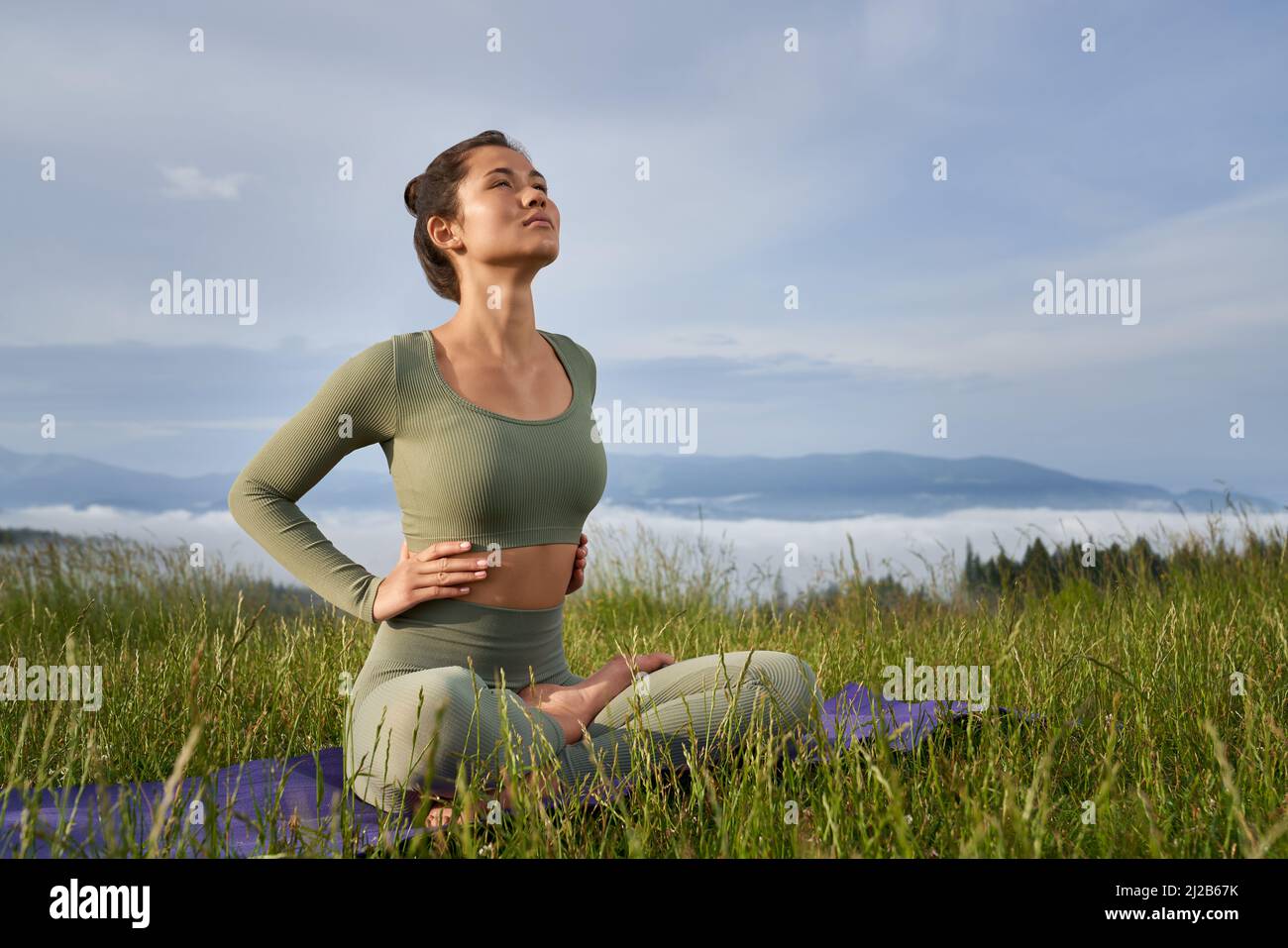 Fitness junge Frau in Sportkleidung genießen Harmonie zwischen grünen Sommer Natur. Aktive Dame, die auf einer Yogamatte sitzt und Übungen für den Körper macht. Stockfoto