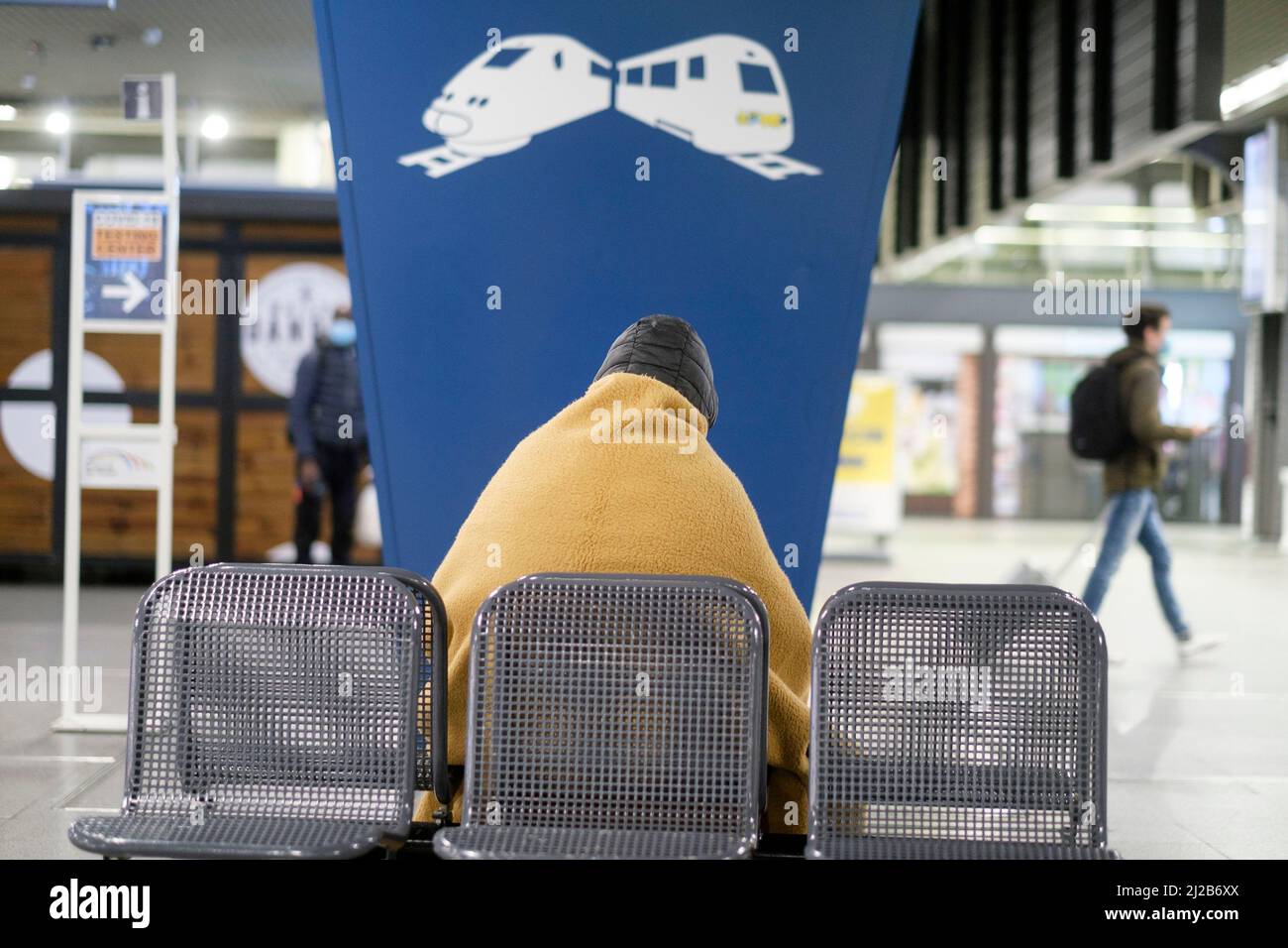 Obdachlose Person von hinten im Bahnhof Brüssel-Süd, Belgien Obdachlose Person mit einer Decke auf dem Rücken, um sich zu schützen / hallo Stockfoto