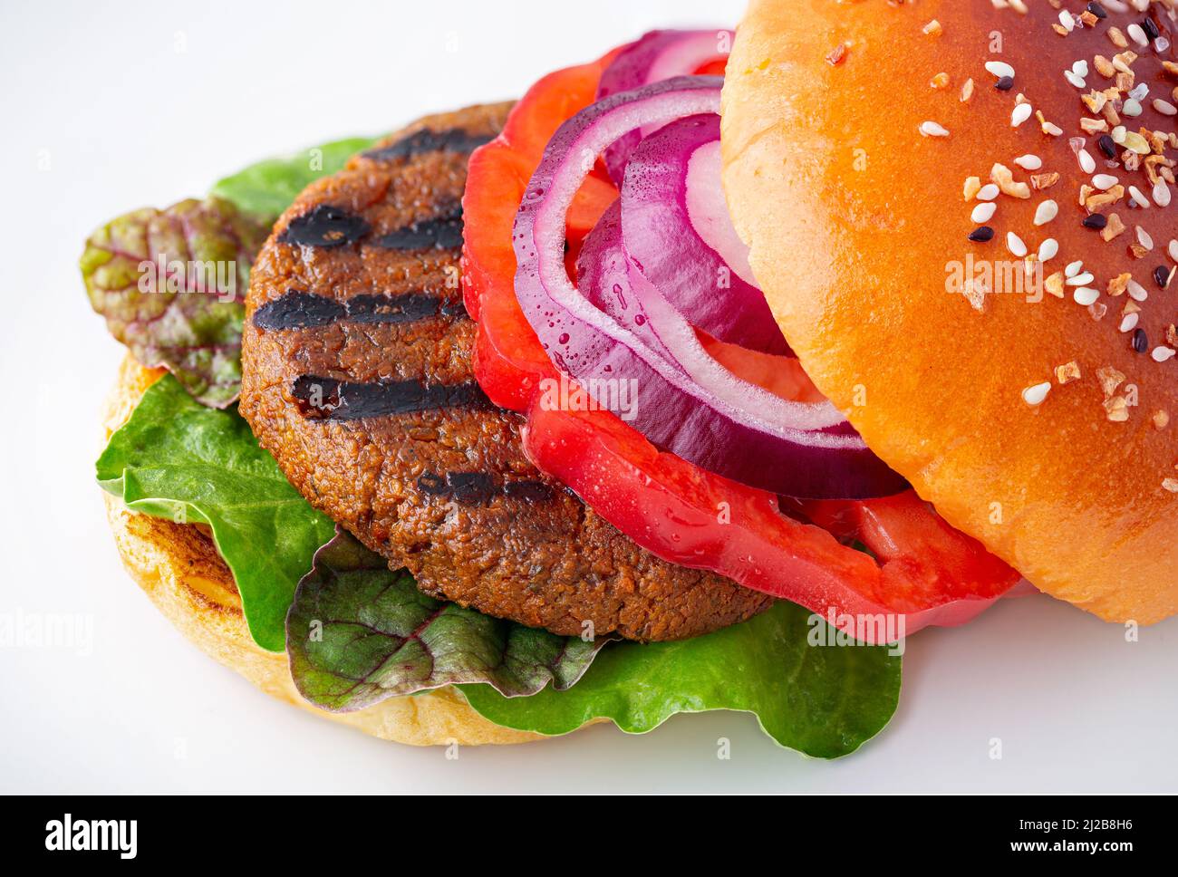 Gesunder vegetarischer gegrillter Veggie-Burger auf Pflanzenbasis mit Blattgemüse, Tomate aus Erbstück, roten Zwiebeln auf einem Brioche-Brötchen, gekrönt mit Samen Stockfoto