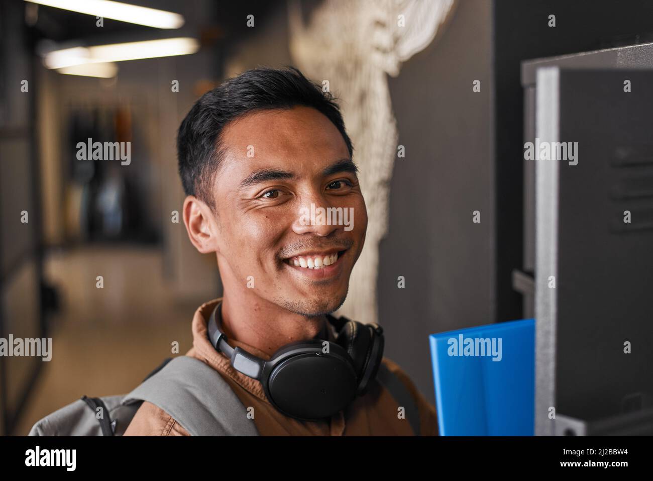 Ein junger südostasiatischer Mann lächelt und nimmt Bücher aus seinem Universitätsfach Stockfoto