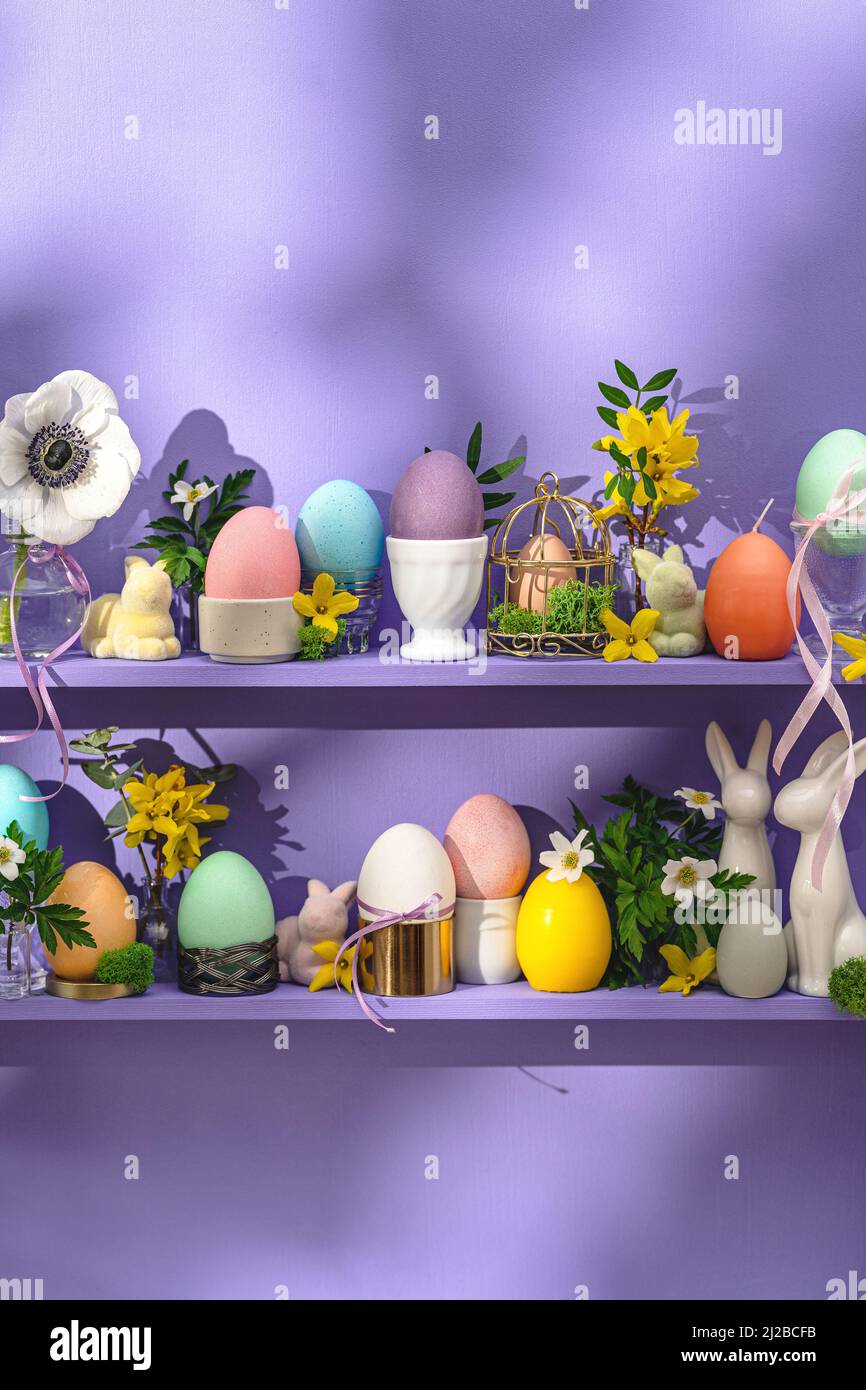 Grußkarte Frohe Ostern. Bunte Eier osterdekoration und Frühlingsblumen auf kleinen violetten Regalen. Stockfoto