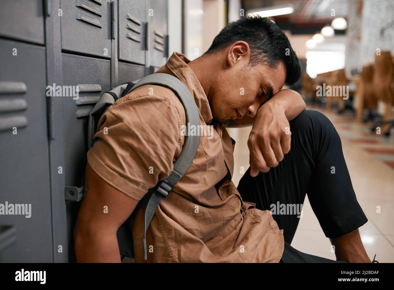 Ein junger südostasiatischer Student lehnt sich auf dem Universitätsgelände auf die Knie Stockfoto