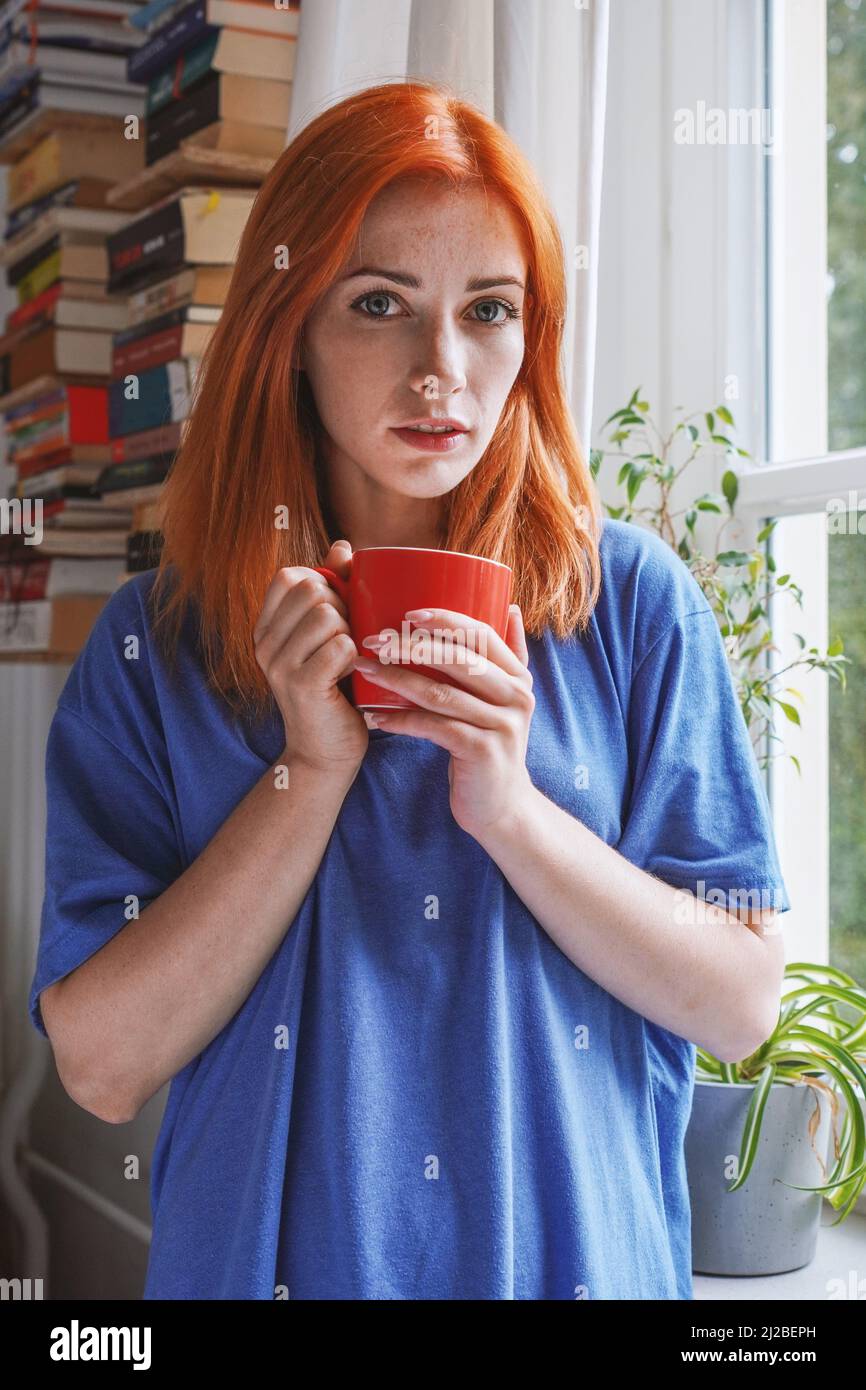 Junge Frau, die zu Hause in ihrem Wohnzimmer mit einer Kaffeetasse steht Stockfoto