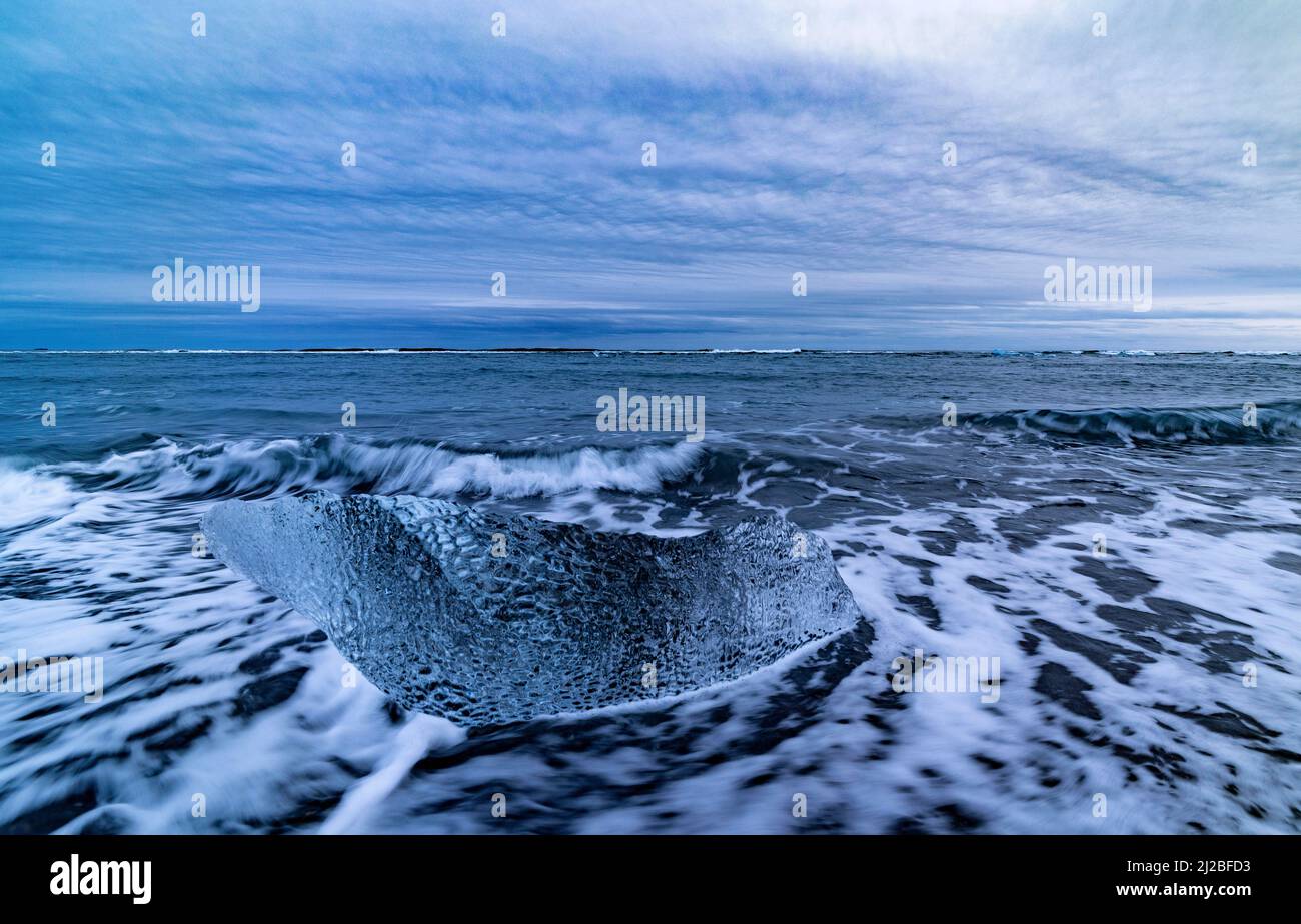Kleine Eisblöcke und ankommende Wellen am Diamond Beach mit schwarzem Sand, Breidamerkursandur, Island Stockfoto