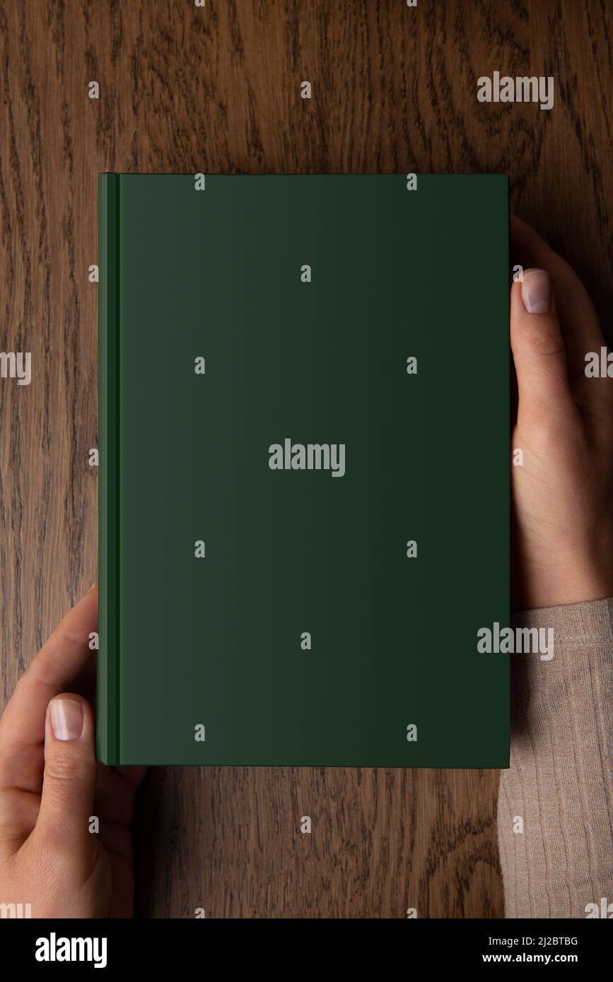 Die Hände einer Frau halten ein Buch mit einem Kopierraum, grün leeres Buchmockup Stockfoto