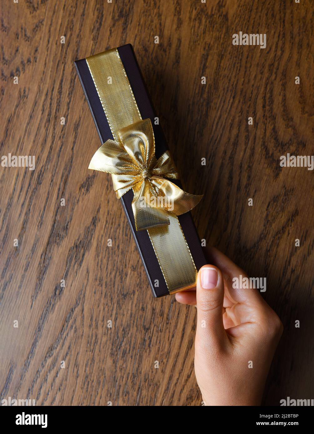 Eine Frauenhand hält eine braune Geschenkbox mit einer goldenen Schleife Stockfoto