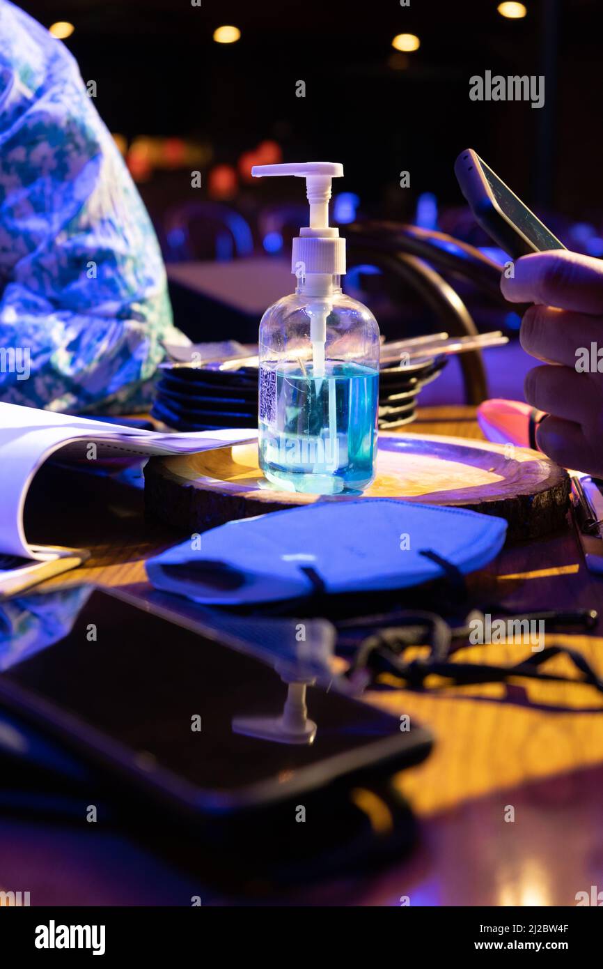Vertikale Aufnahme mit blauem Händedesinfektionsmittel, das auf dem Menü ruht, während Menschen während der COVID-Pandemie des Coronavirus in der Nähe Handys benutzen Stockfoto