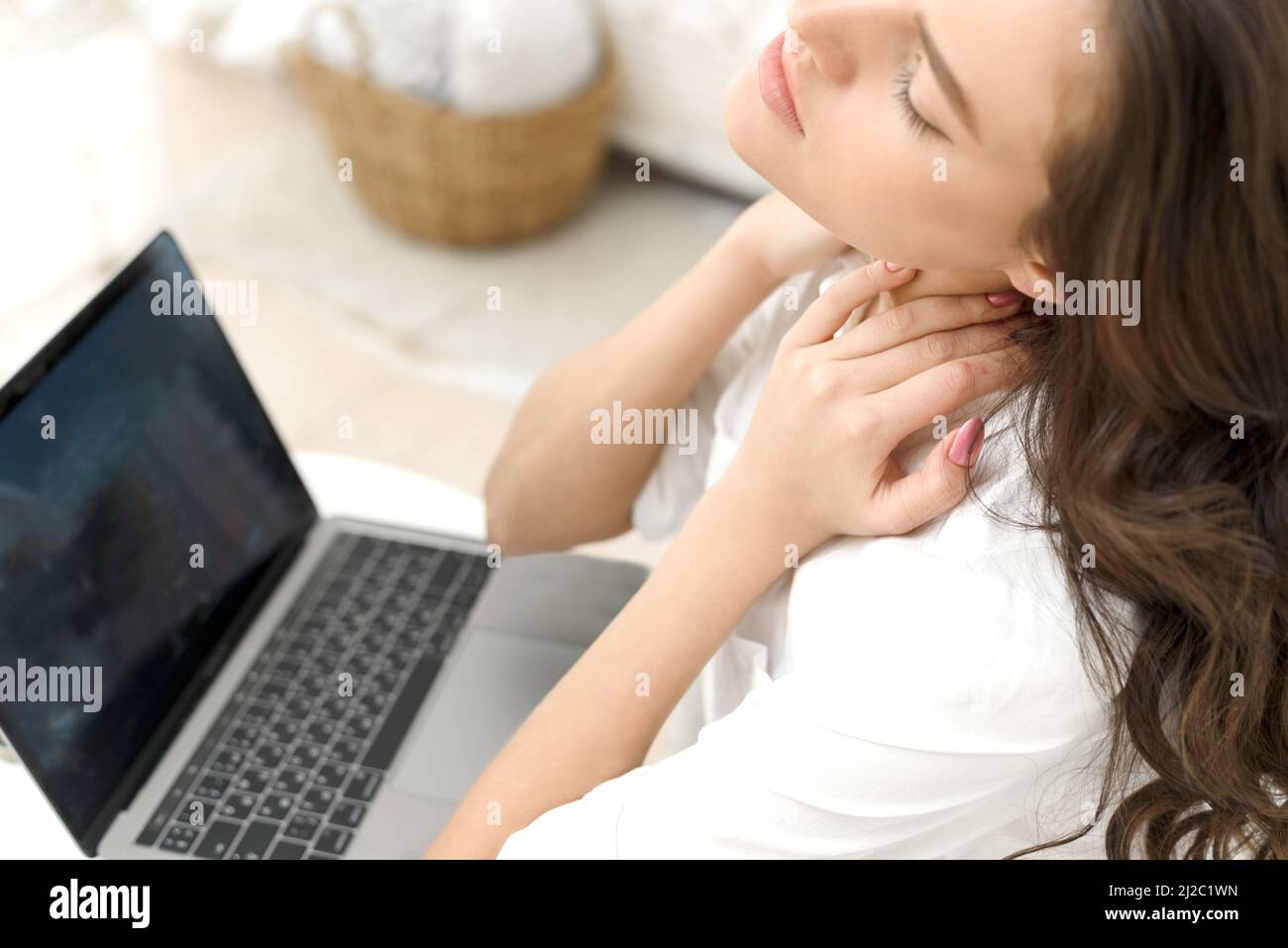 Müde junge Frau mit Nackenschmerzen, die im Büro zu Hause in einem Laptop arbeitet. Müde junge Frau berührt ihren steifen Hals, fühlt Gelenkschmerzen, Rückenschmerzen, massiert Stockfoto