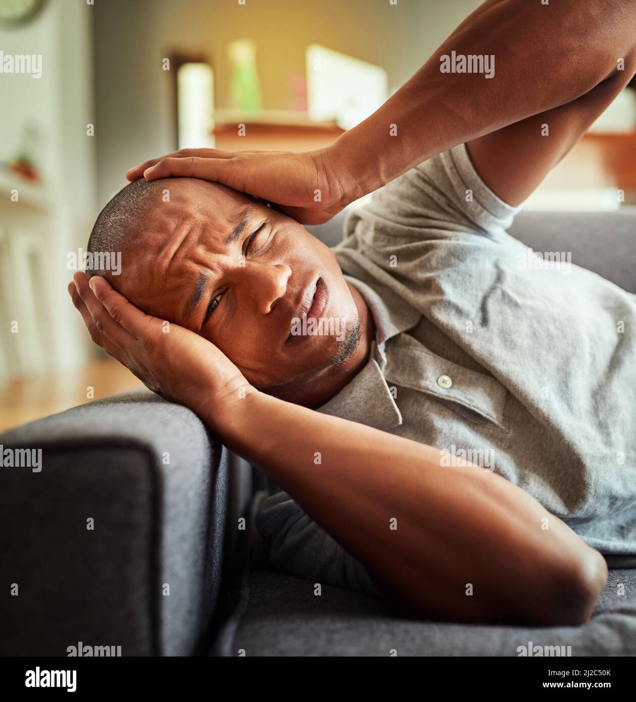 Mein Gehirn kann es nicht mehr ertragen. Aufnahme eines gestressten jungen Mannes, der tagsüber zu Hause auf einer Couch lag und seinen Kopf in Unannehmlichkeiten hielt. Stockfoto