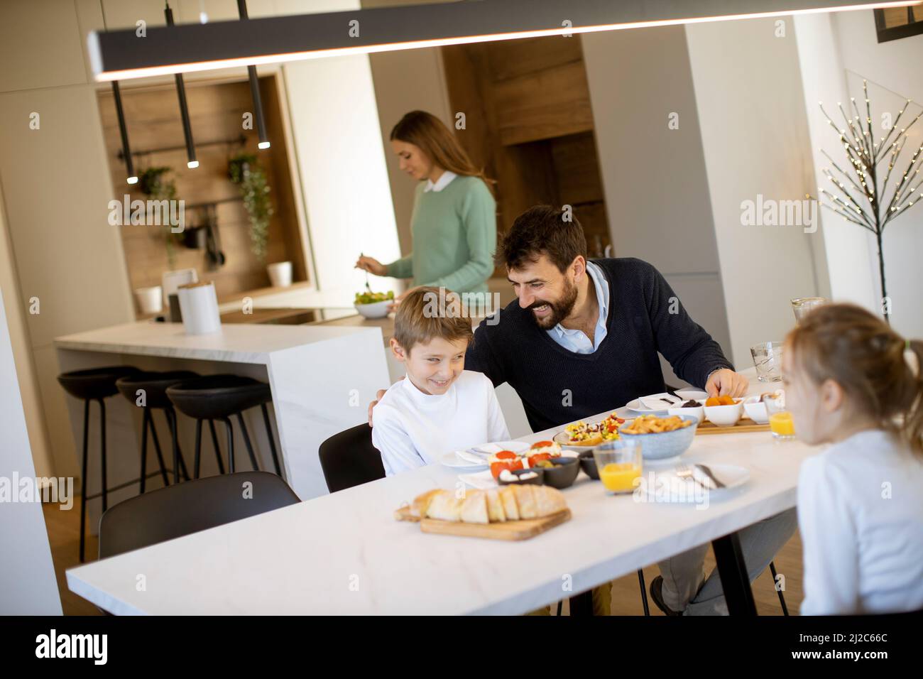 Junge glückliche Familie, die beim Frühstück am Esstisch im Apartment sprach Stockfoto