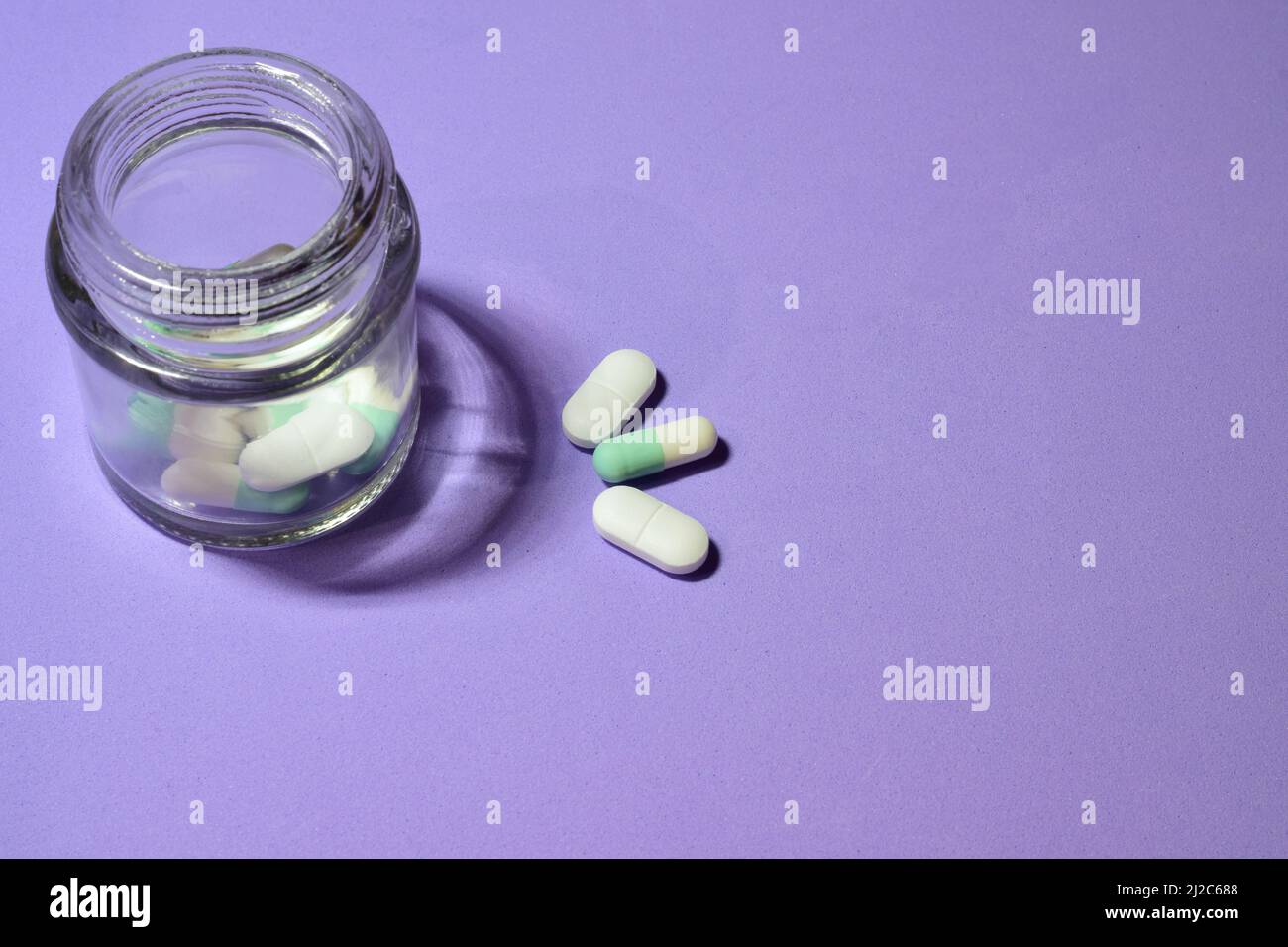 Einige Pillen und ein kleines Glas auf einem violetten Hintergrund Stockfoto