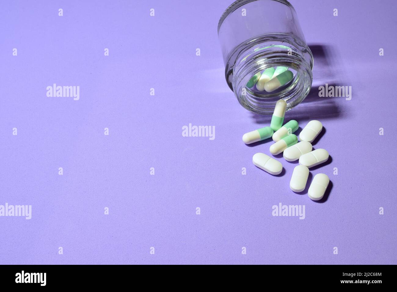 Einige Pillen und ein kleines Glas auf einem violetten Hintergrund Stockfoto