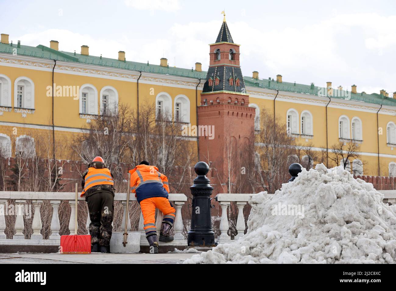 Zwei Arbeiter mit Schaufeln stehen auf dem Hintergrund des Moskauer Kremls. Arbeitsmigranten während der Ruhezeit, Straßenreinigung im Frühjahr, Schneeräumung Stockfoto