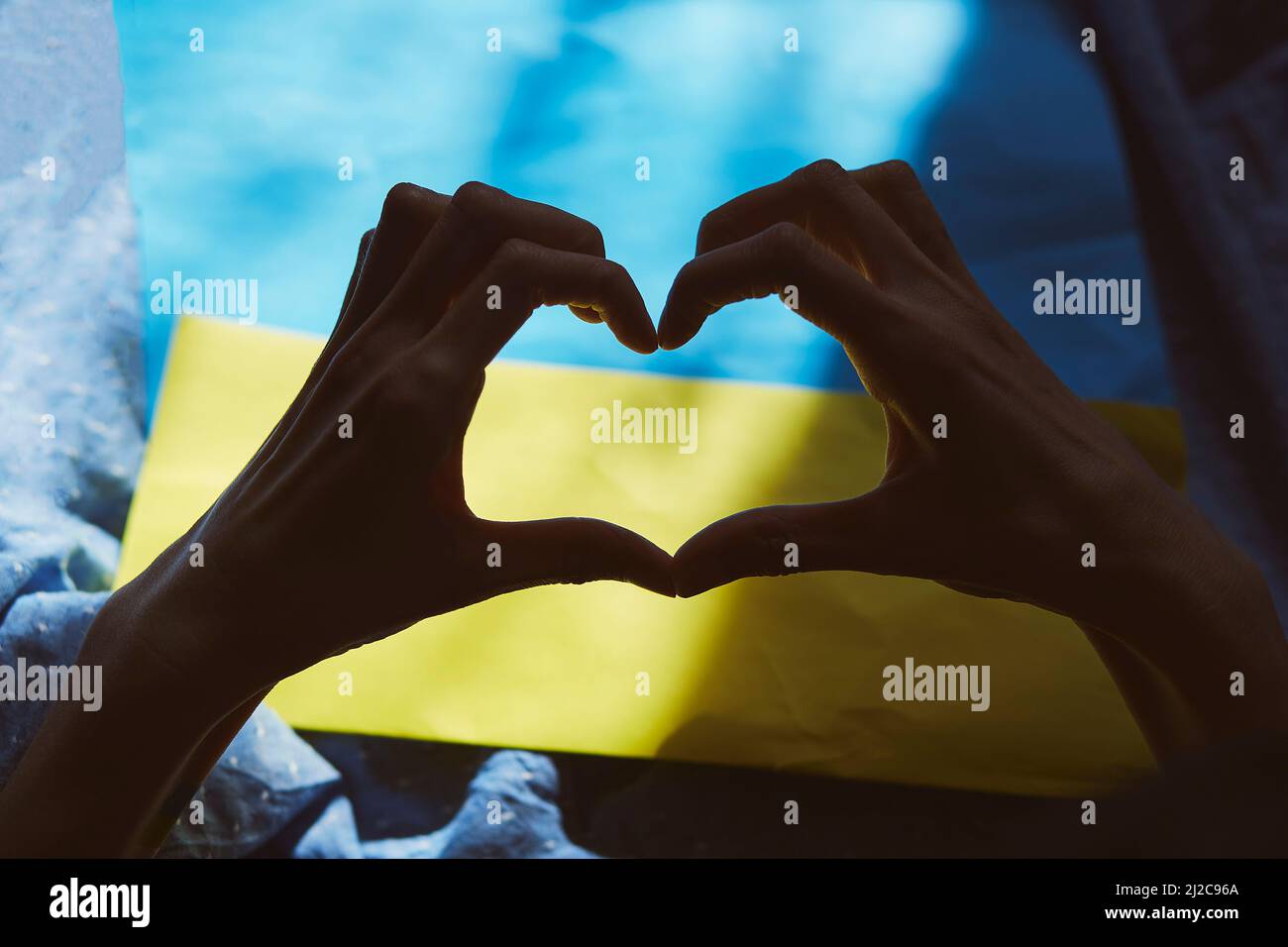 Herzförmige Hände auf ukrainischer Flagge mit Schatten. Prioritätsfrage. Aktuelle Nachrichten. Ukrainische Flagge, kreativer patriotischer Hintergrund. Beendet den Krieg in der Ukraine. Stoppt die russische Aggression Stockfoto