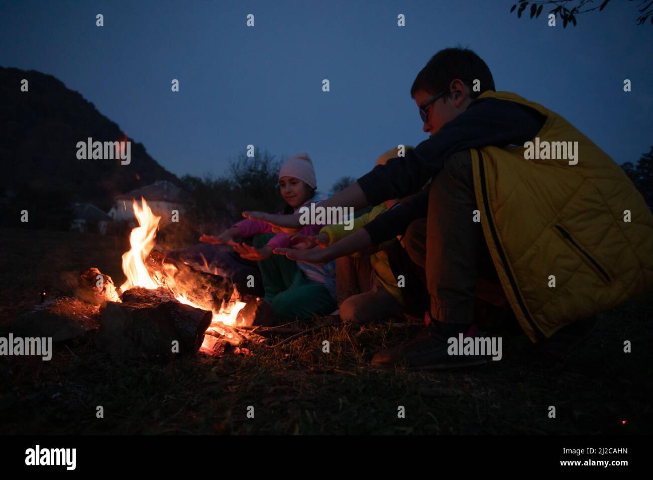 Kinder nach dem Wandern machen ein Picknick - eine Gruppe von glücklichen Freunden, die am Lagerfeuer Würstchen braten Stockfoto