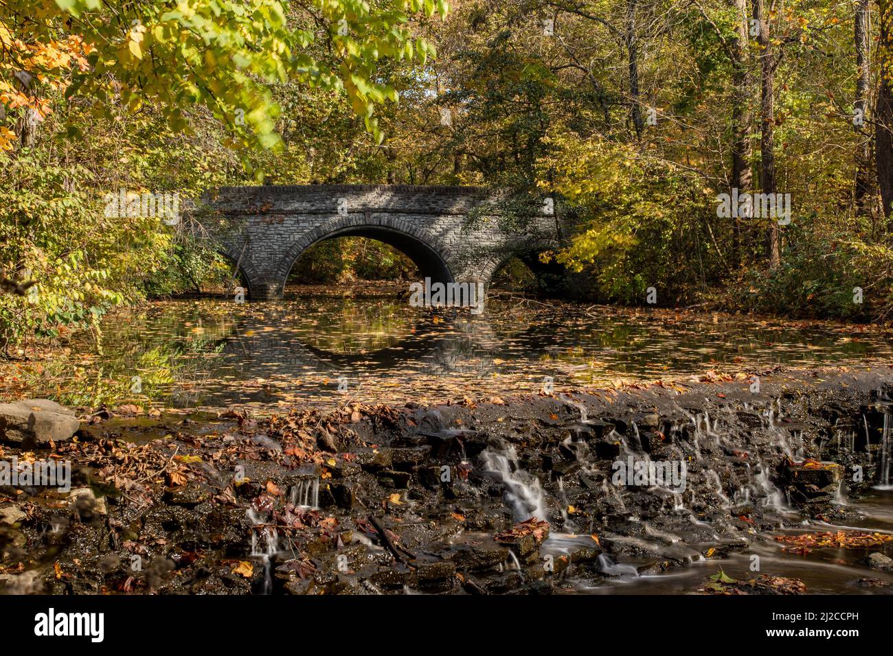 Herbstbäume und Farben rund um einen Wasserfall und eine Brücke auf Sharon Creek. Sharon Woods Metro Park, Sharonville, Cincinnati, Ohio, USA. Stockfoto