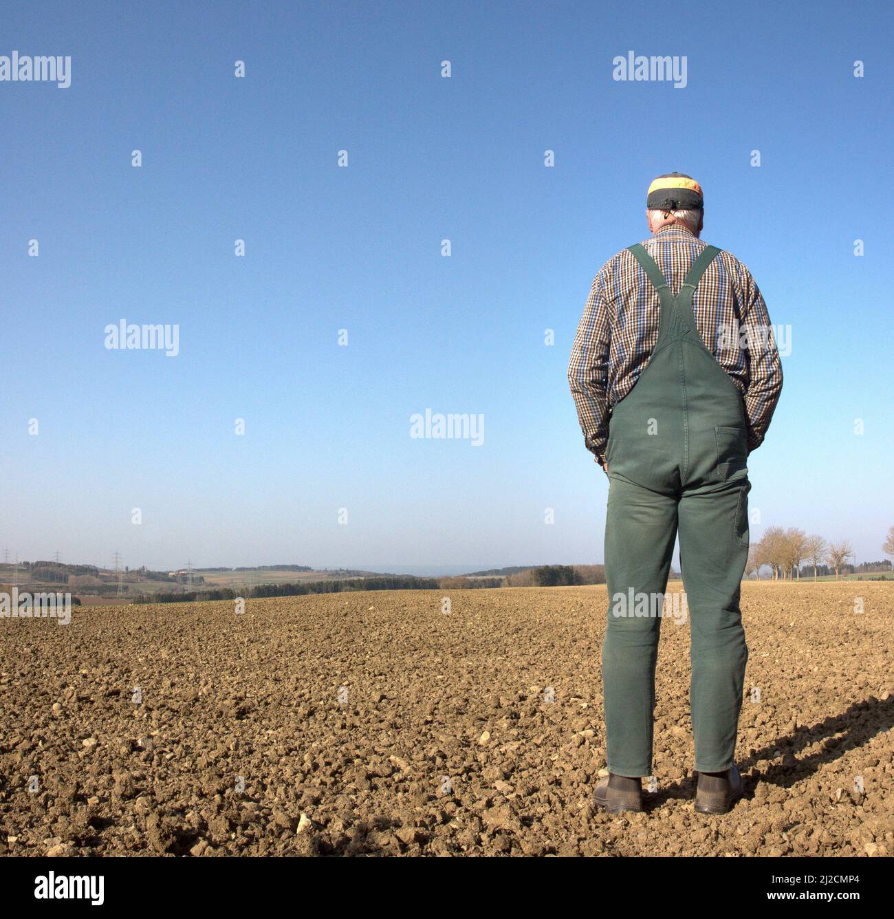 Ein Bauer steht an einem glorreichen Frühlingstag auf seinem trockenen Feld und sorgt sich um den neu gesät Samen. Stockfoto