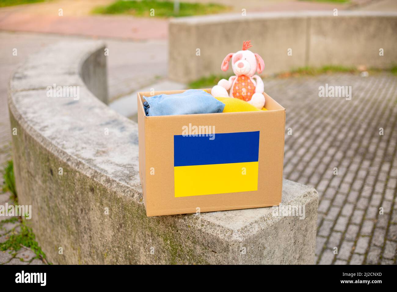 Eine Kiste mit ukrainischer Flagge für die Spende humanitärer Hilfe mit Dingen und Kinderspielzeug für ukrainische Flüchtlinge auf der Straße. Bleiben Sie in der Ukraine. Stockfoto